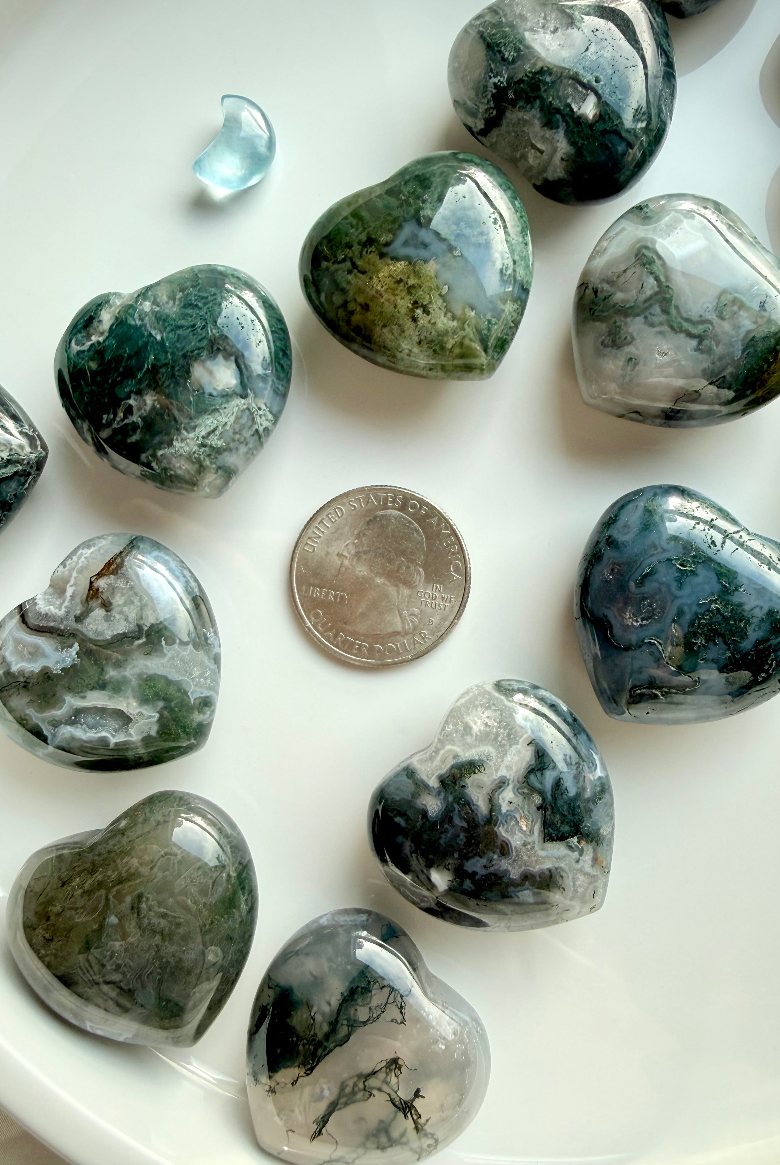 Moss Agate hearts next to a quarter for size reference, showing polished green and grey crystal patterns