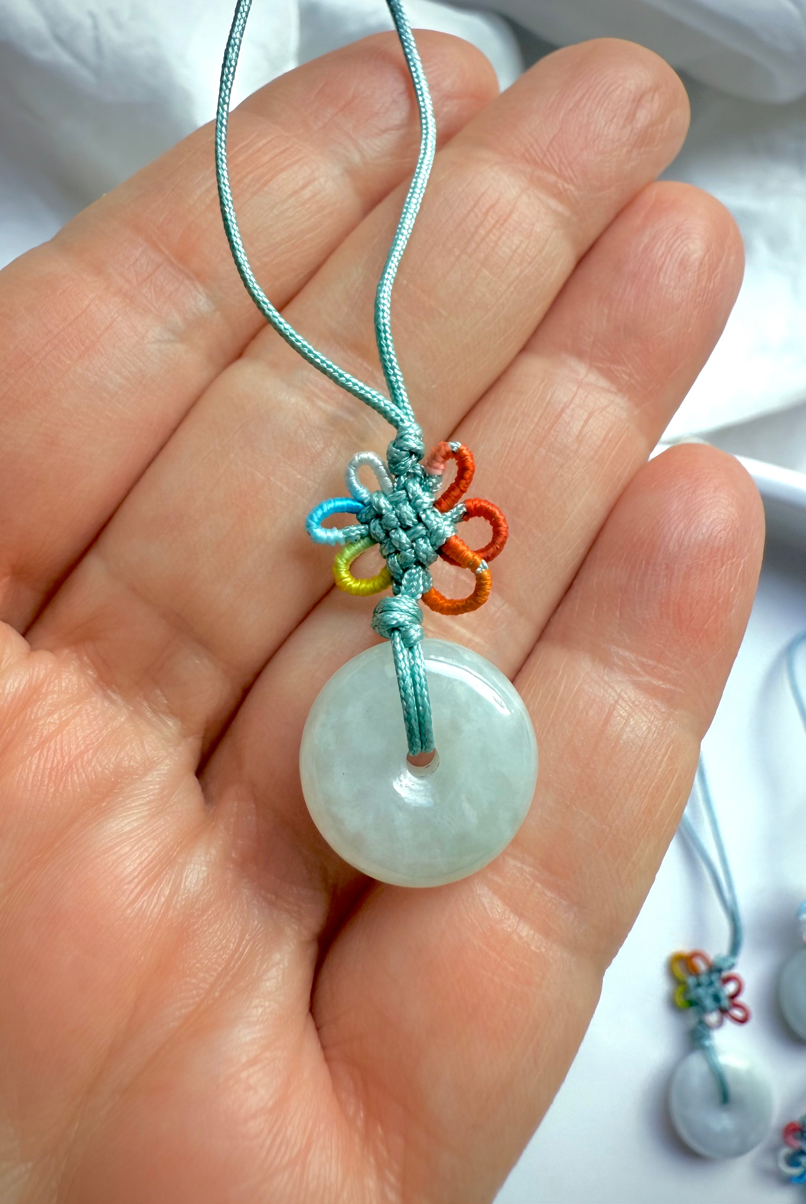 Closeup of hand holding jade peace buckle charm with rainbow lucky knot and satin green cord