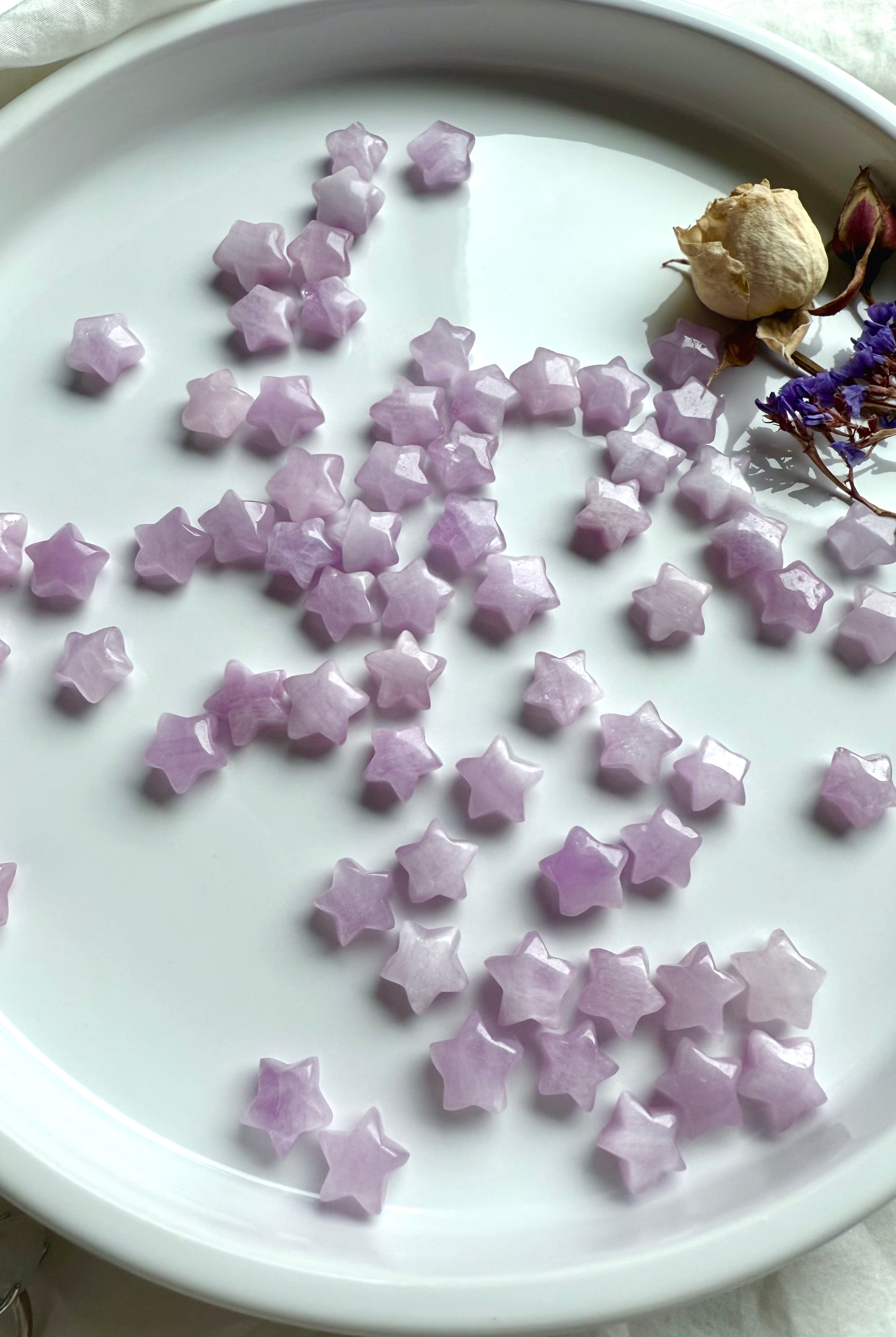 Dozens of glossy Kunzite stars on a white surface, tiny polished carvings for emotional healing and sacred rituals.
