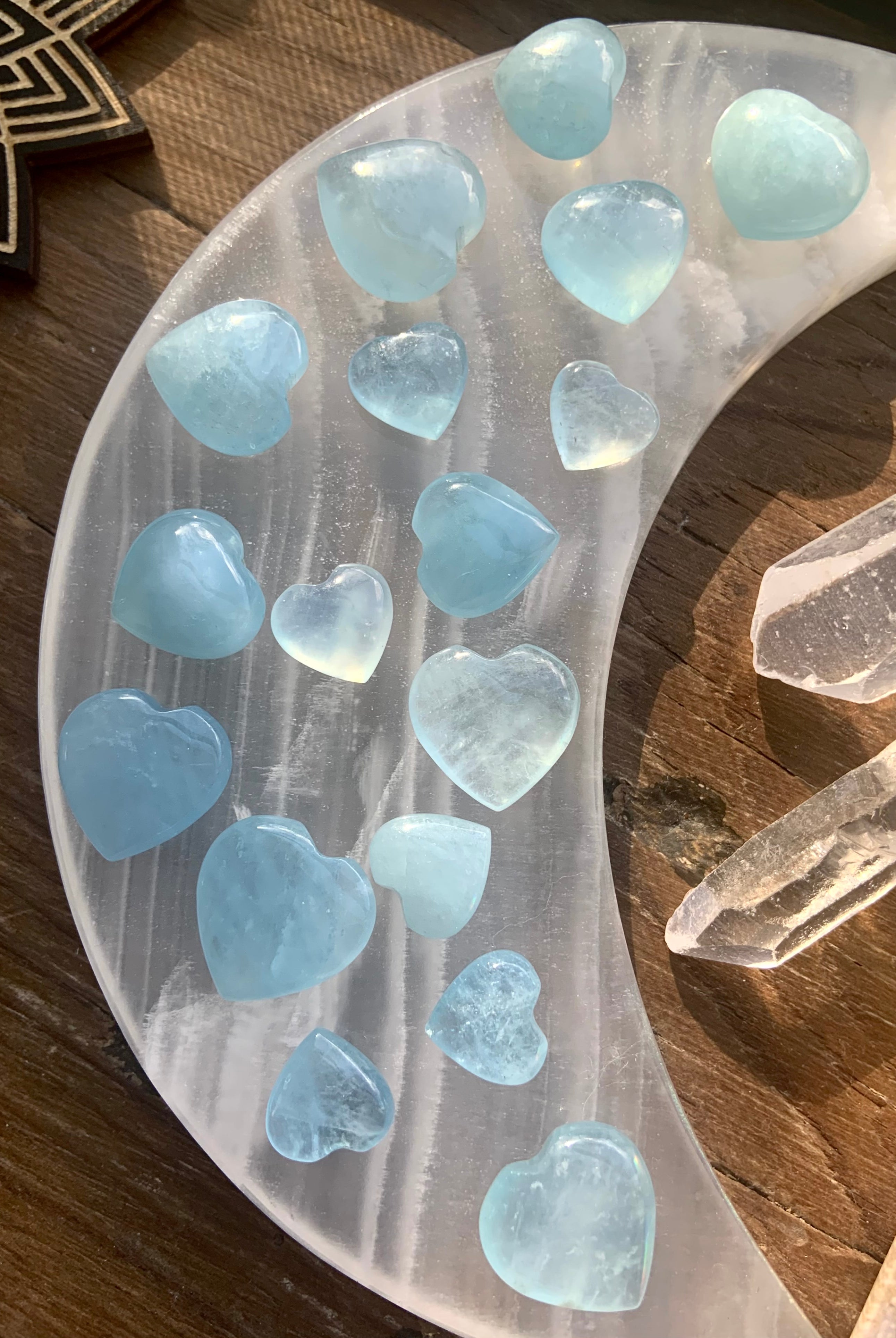 Overhead view of luminous Aquamarine crystal hearts arranged on a white stone moon plate with quartz points — soothing blue healing stones for calm + clarity.
