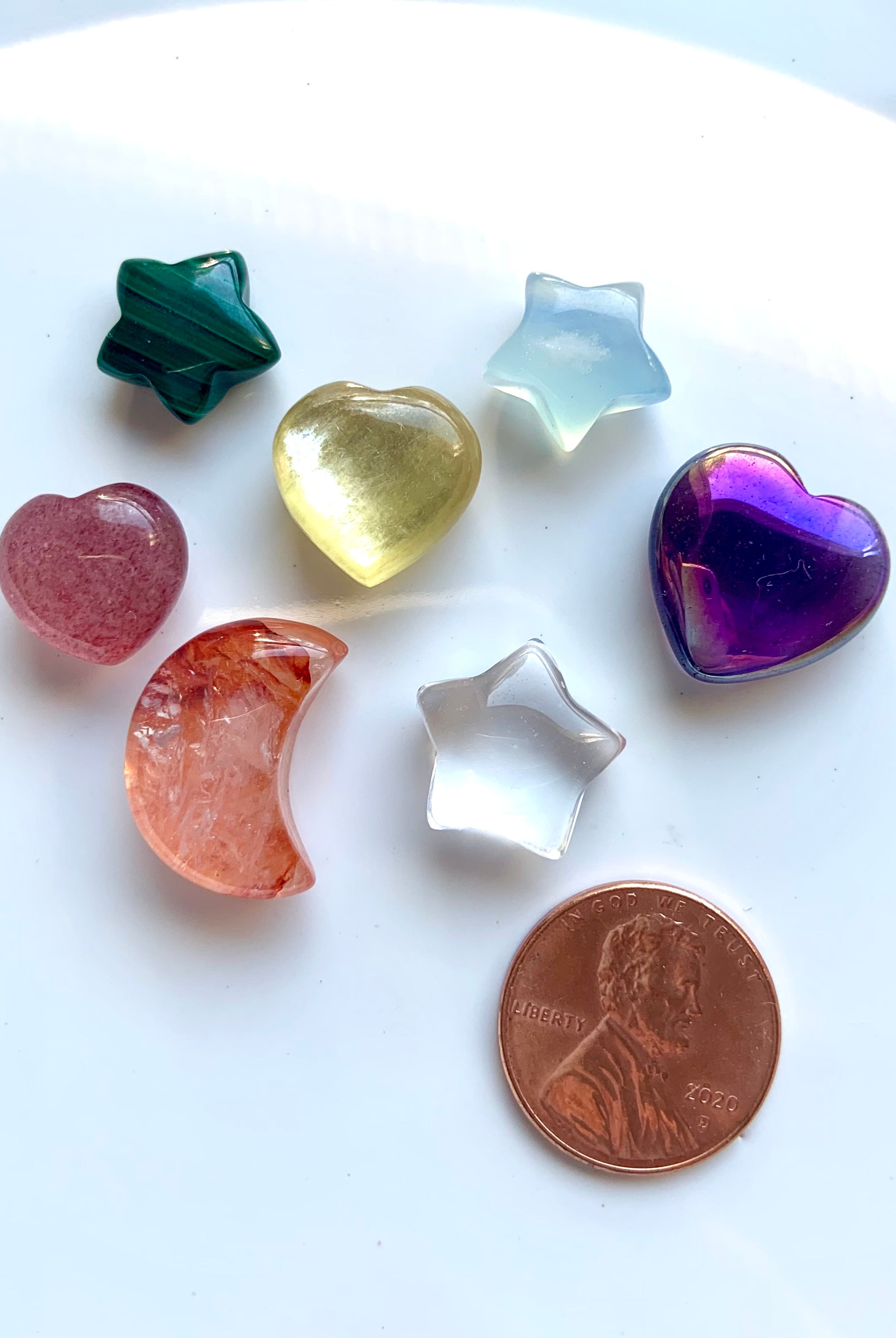 7 mini carved chakra crystals — hearts, stars & moon — shown with a penny for size comparison
