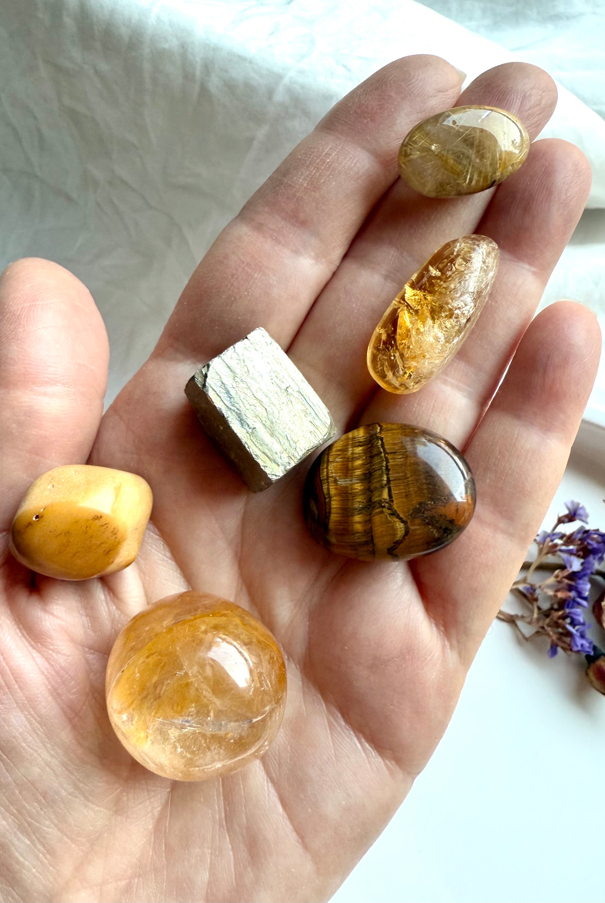 Golden healer, citrine, golden rutile, tiger’s eye, yellow mookaite, and pyrite crystals shown in hand for scale