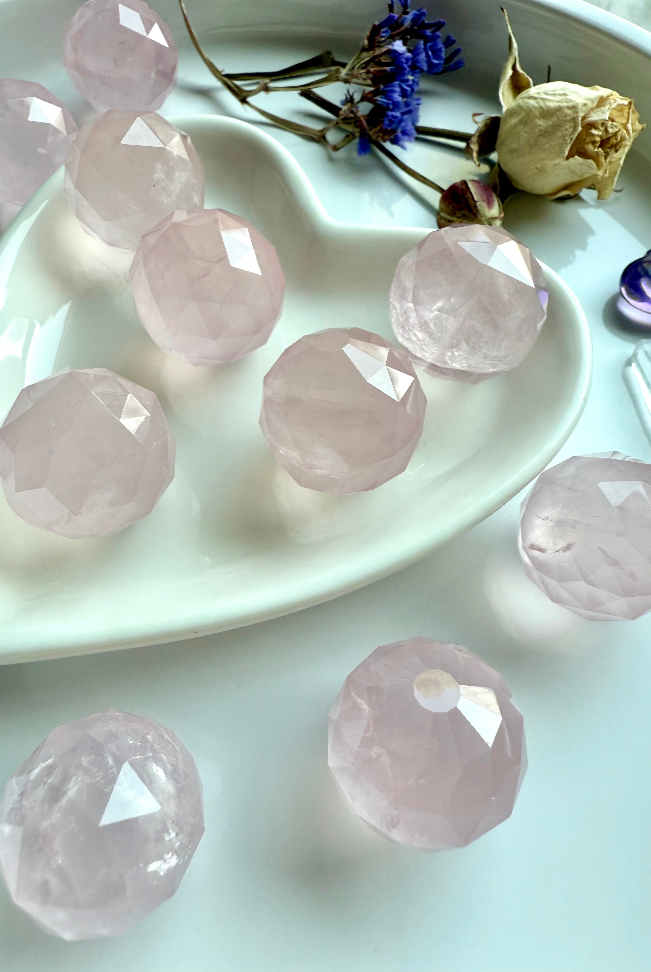 Faceted pink crystals on a white plate with dried flowers. Heart chakra stones for unconditional love.