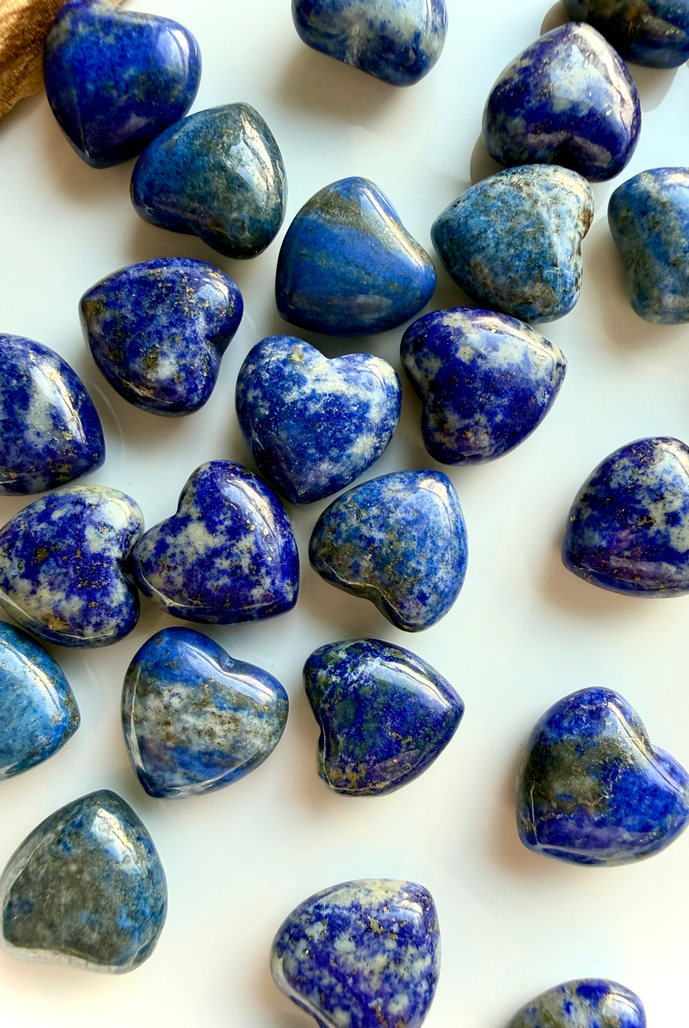 Mini Lapis Lazuli heart crystals scattered on a white surface, polished gemstone hearts highlighting natural color and texture differences