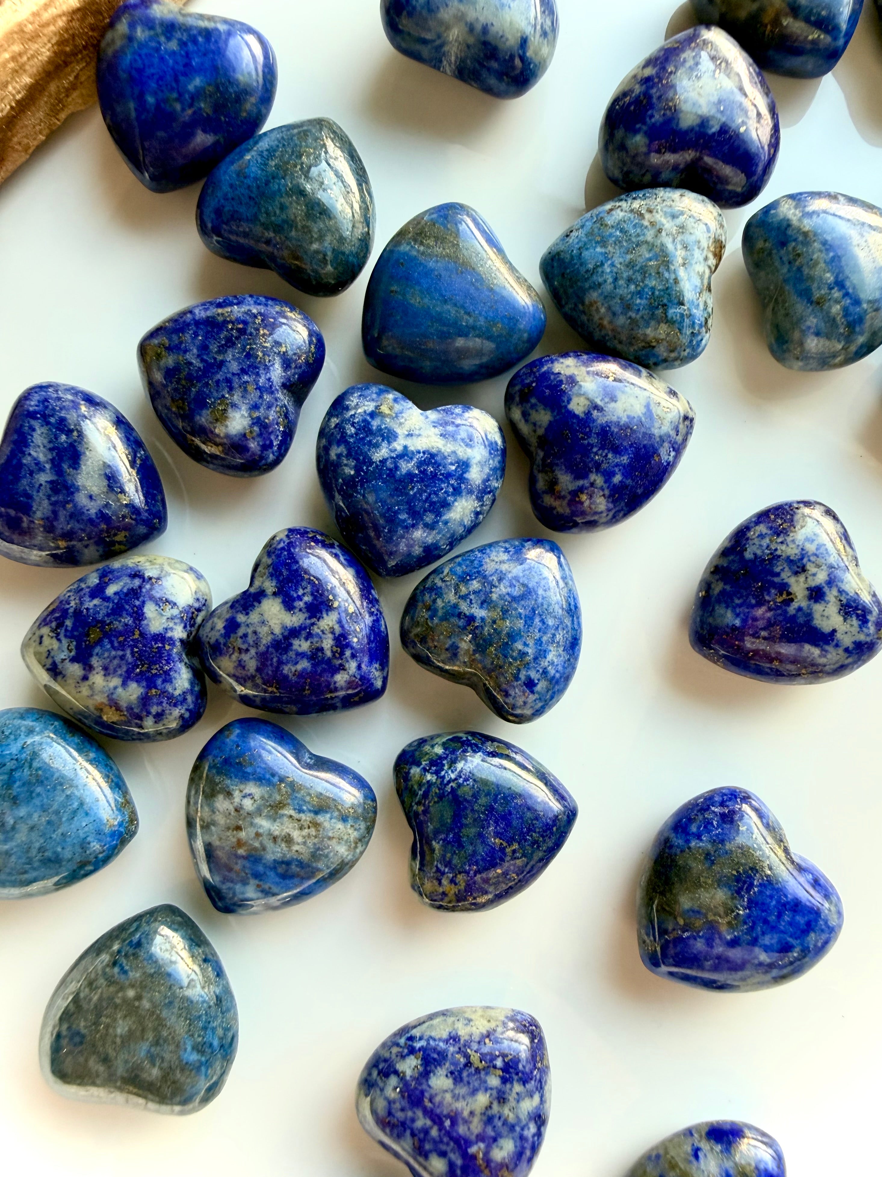 Mini Lapis Lazuli heart crystals scattered on a white surface, polished gemstone hearts highlighting natural color and texture differences