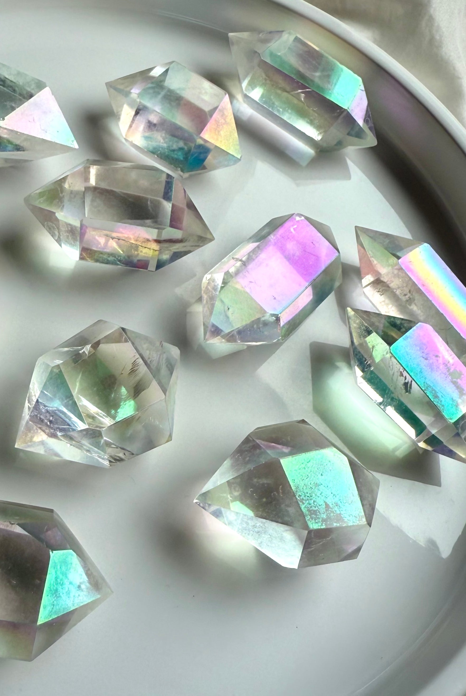 Angel Aura Quartz double terminated points in a circular display dish, glowing with rainbow light for moon rituals and altar décor