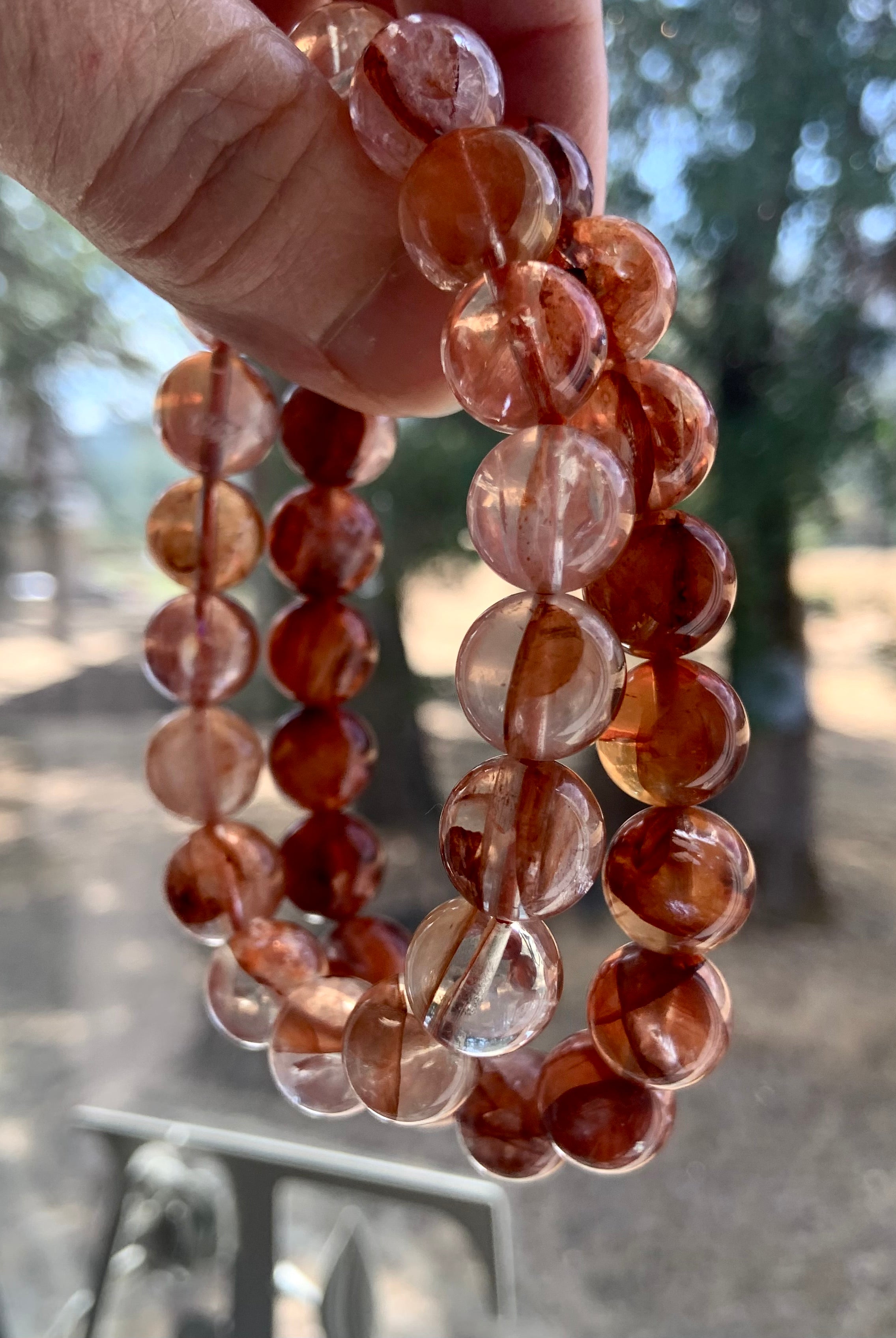 Two Fire Quartz bracelets held up to show color variation between light and dark red quartz options