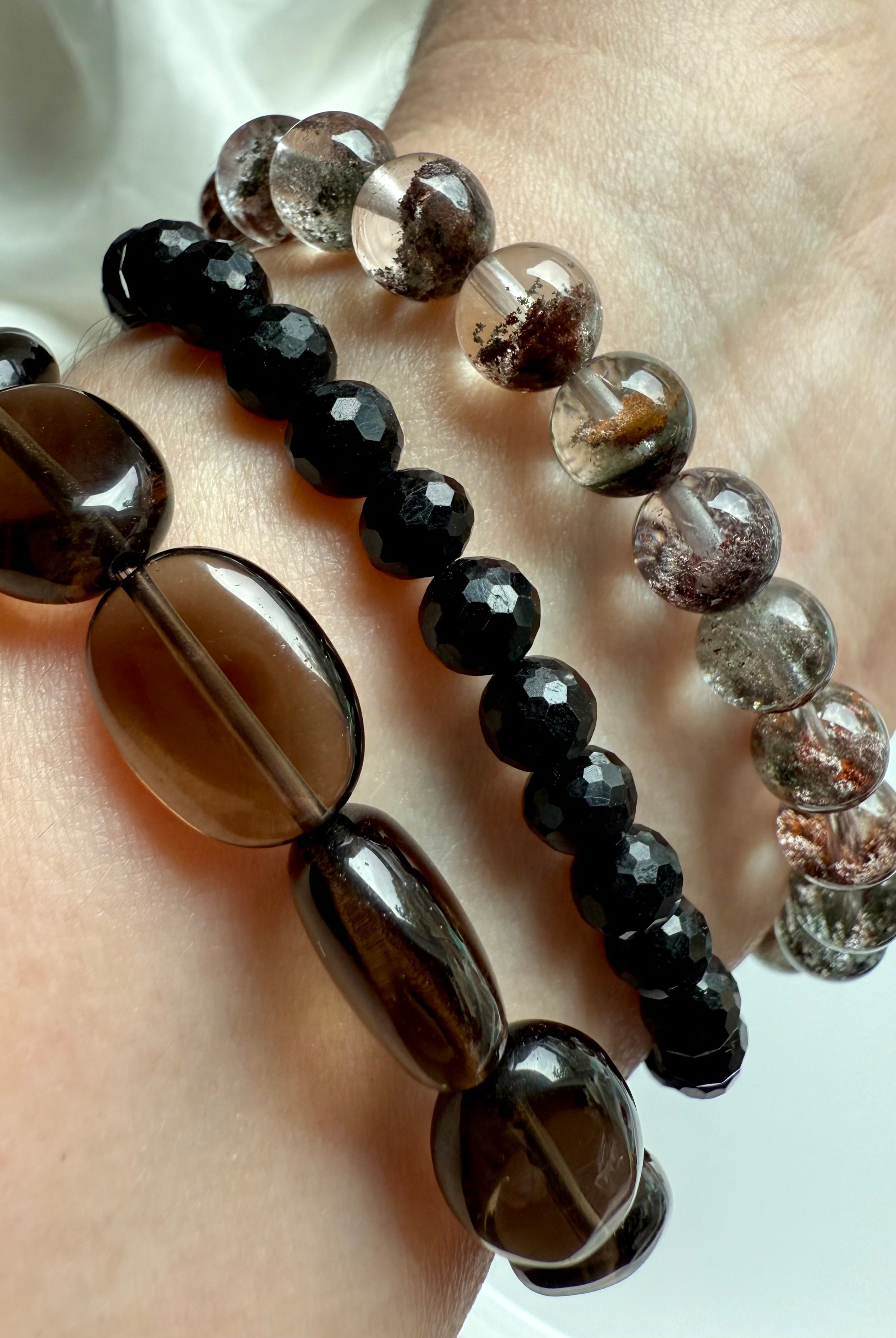 stack of black tourmaline, smoky quartz, and garden quartz crystal bracelets on wrist, showcasing grounding protection and earthy clarity