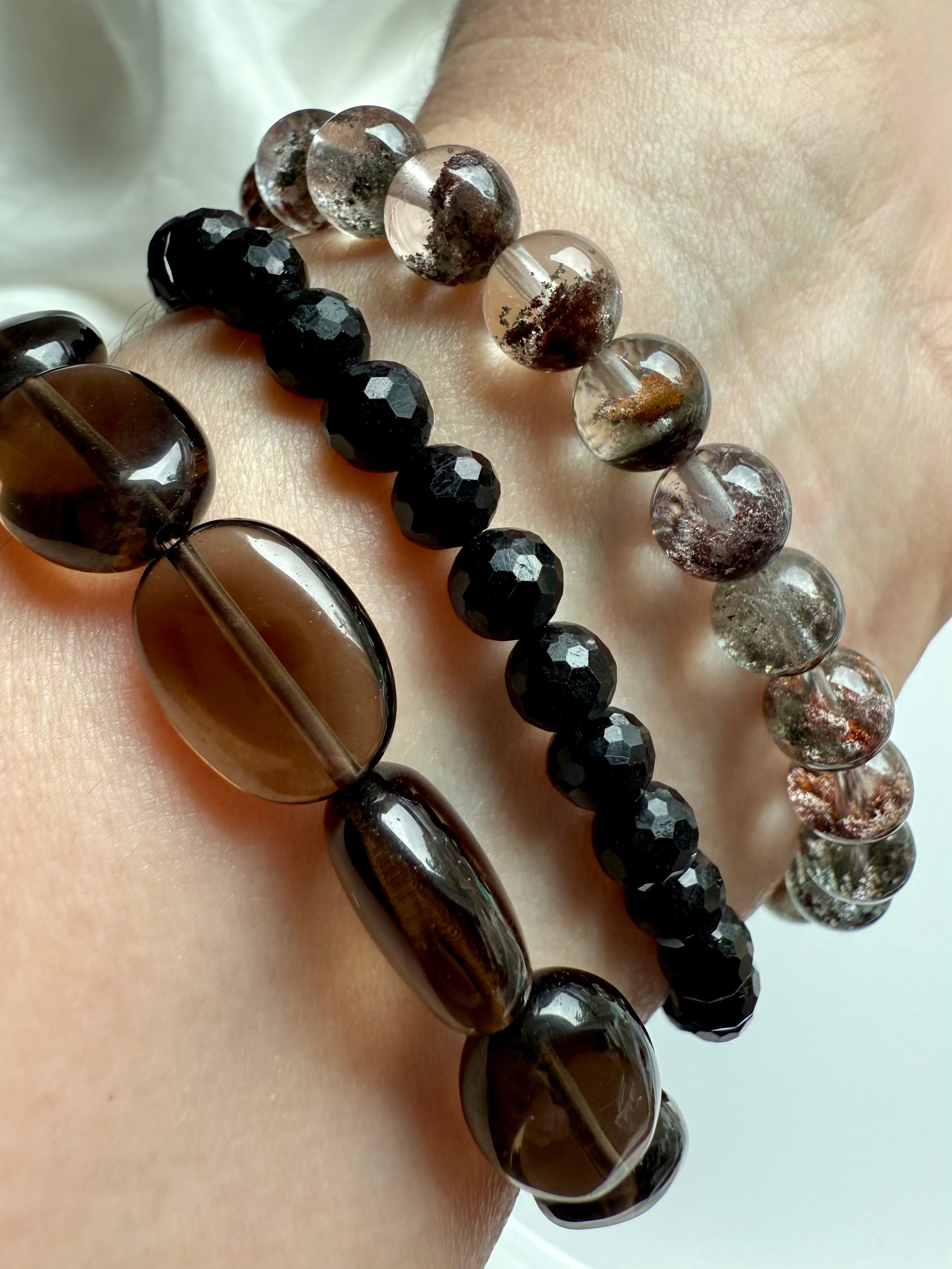 stack of black tourmaline, smoky quartz, and garden quartz crystal bracelets on wrist, showcasing grounding protection and earthy clarity
