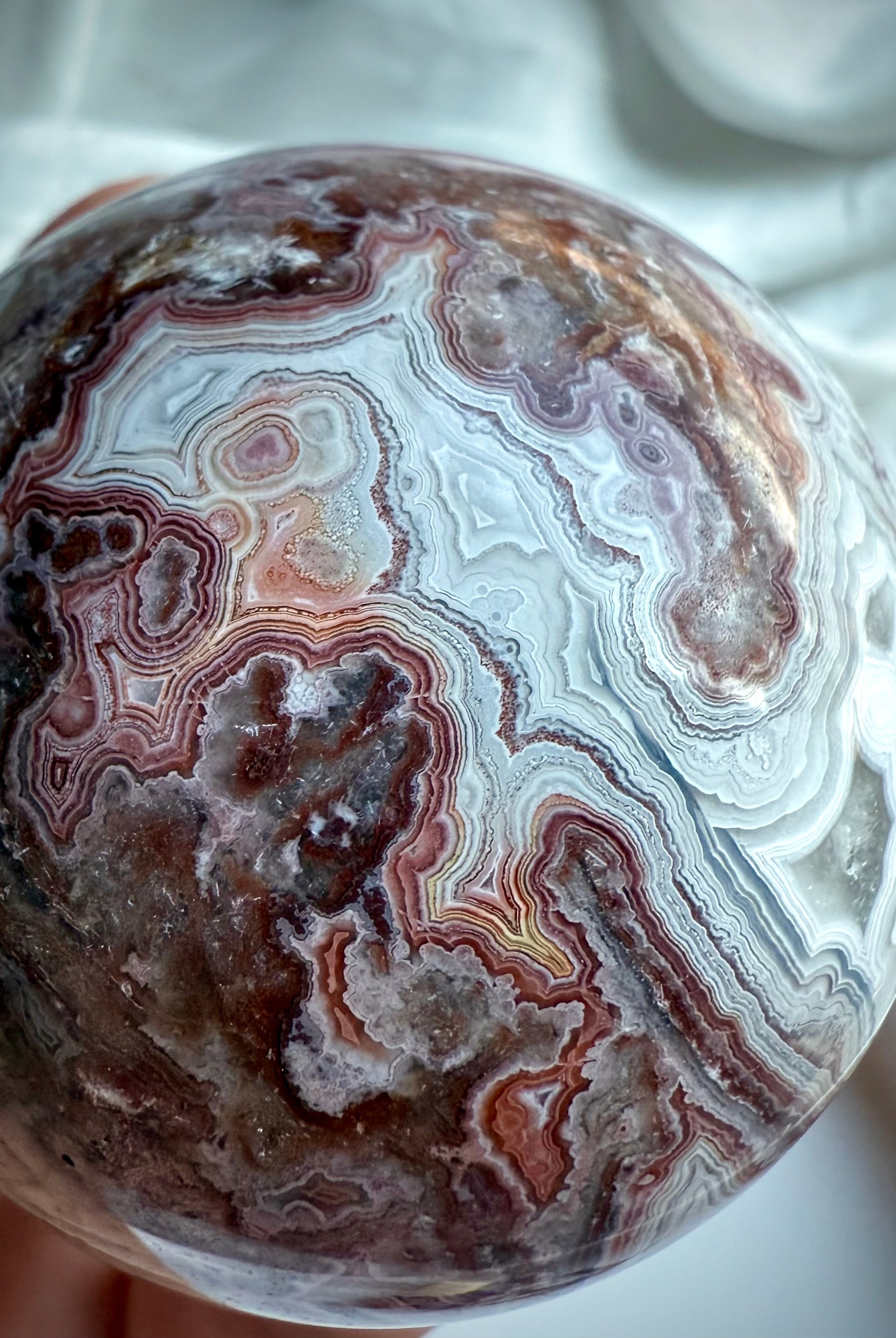 Crazy Lace Agate sphere featuring swirling lace-like patterns in earthy red, gray, and cream tones