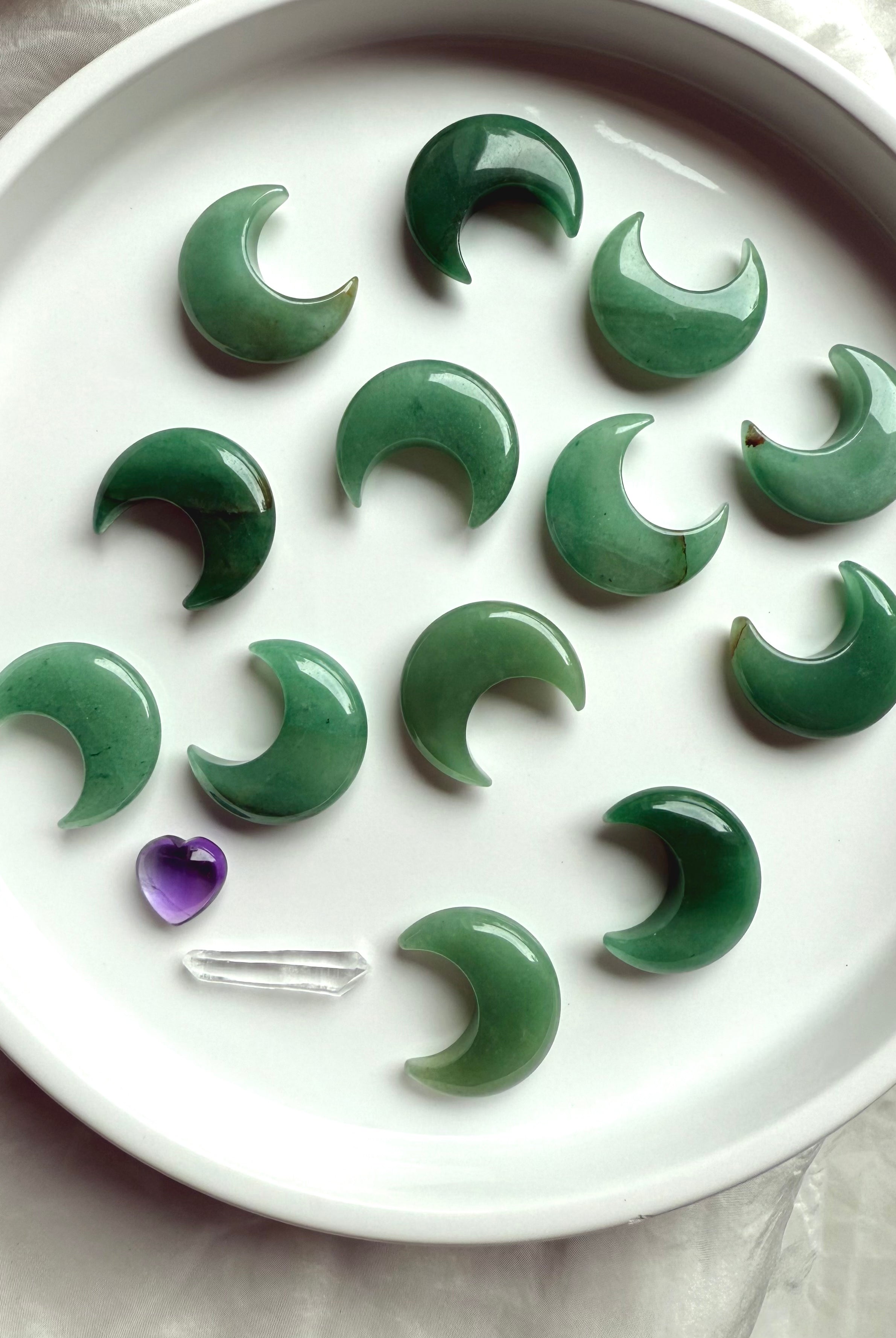 Flatlay of Green Aventurine crescent moons on a white plate with amethyst heart and clear quartz point, Heart Chakra crystal carvings for love and abundance