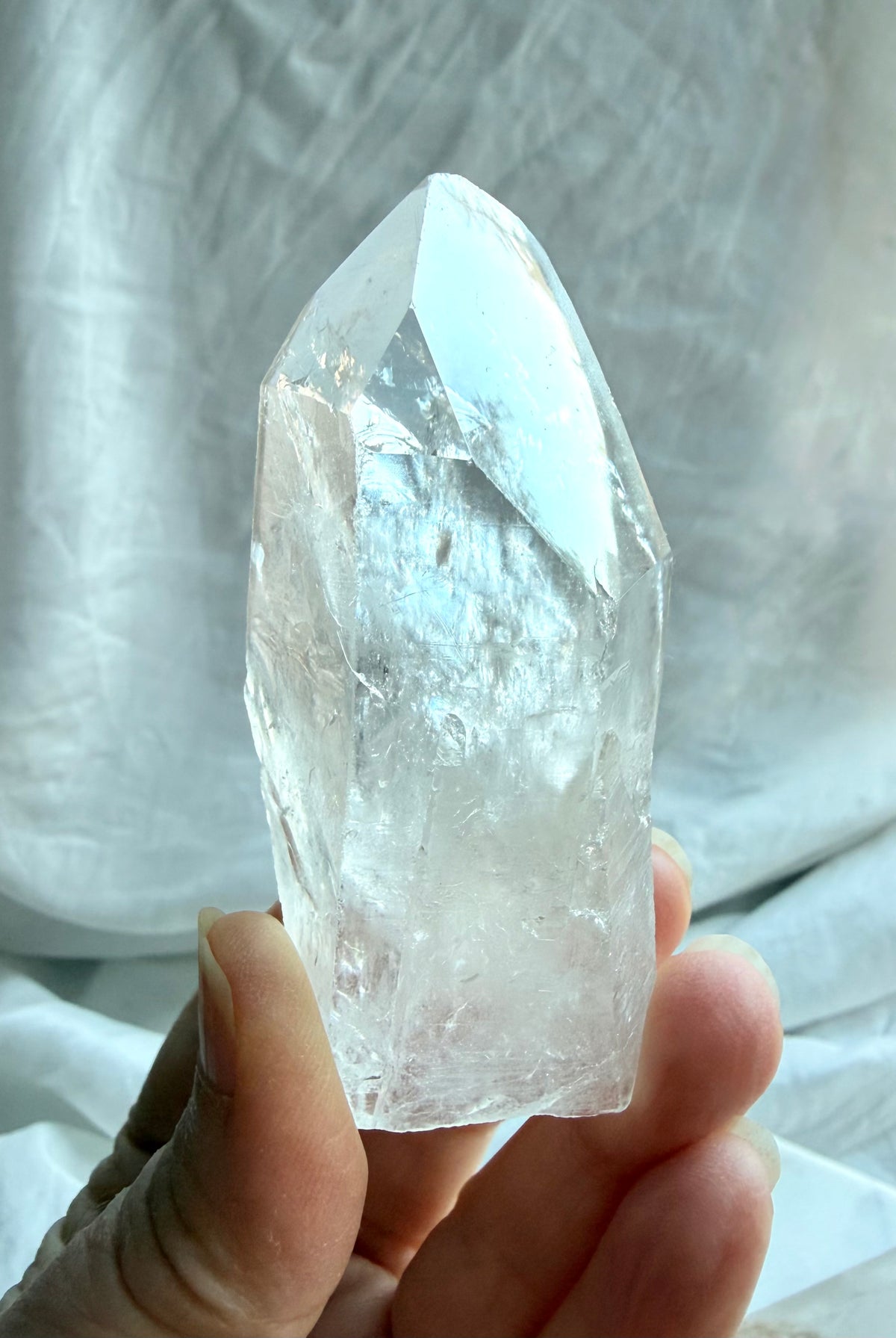 Brazilian Lemurian Quartz point held in hand with textured growth lines, cloudy veils, and a naturally formed termination
