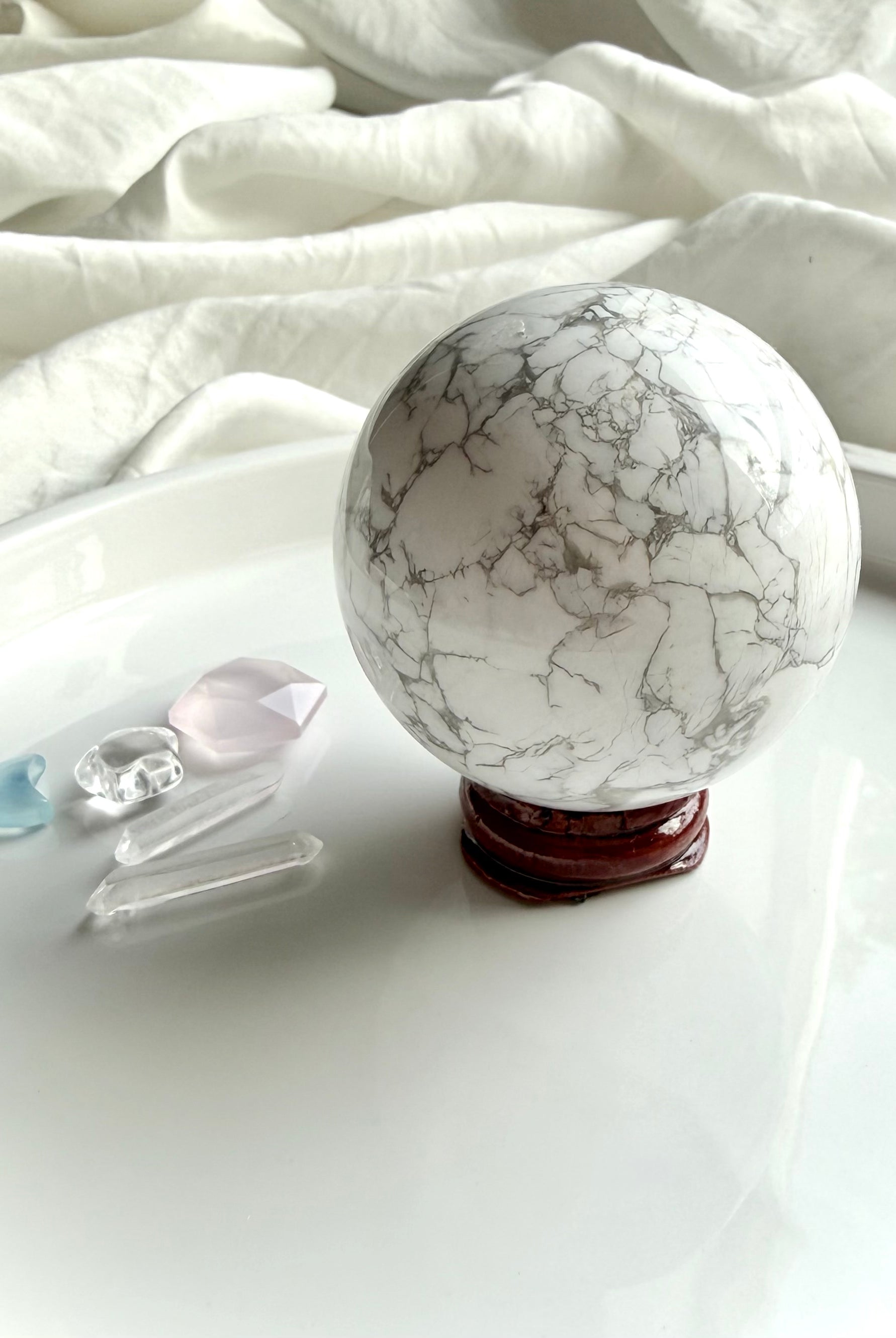 Howlite crystal sphere on wooden stand with rose quartz and clear quartz accents, calming stone for emotional healing and sleep