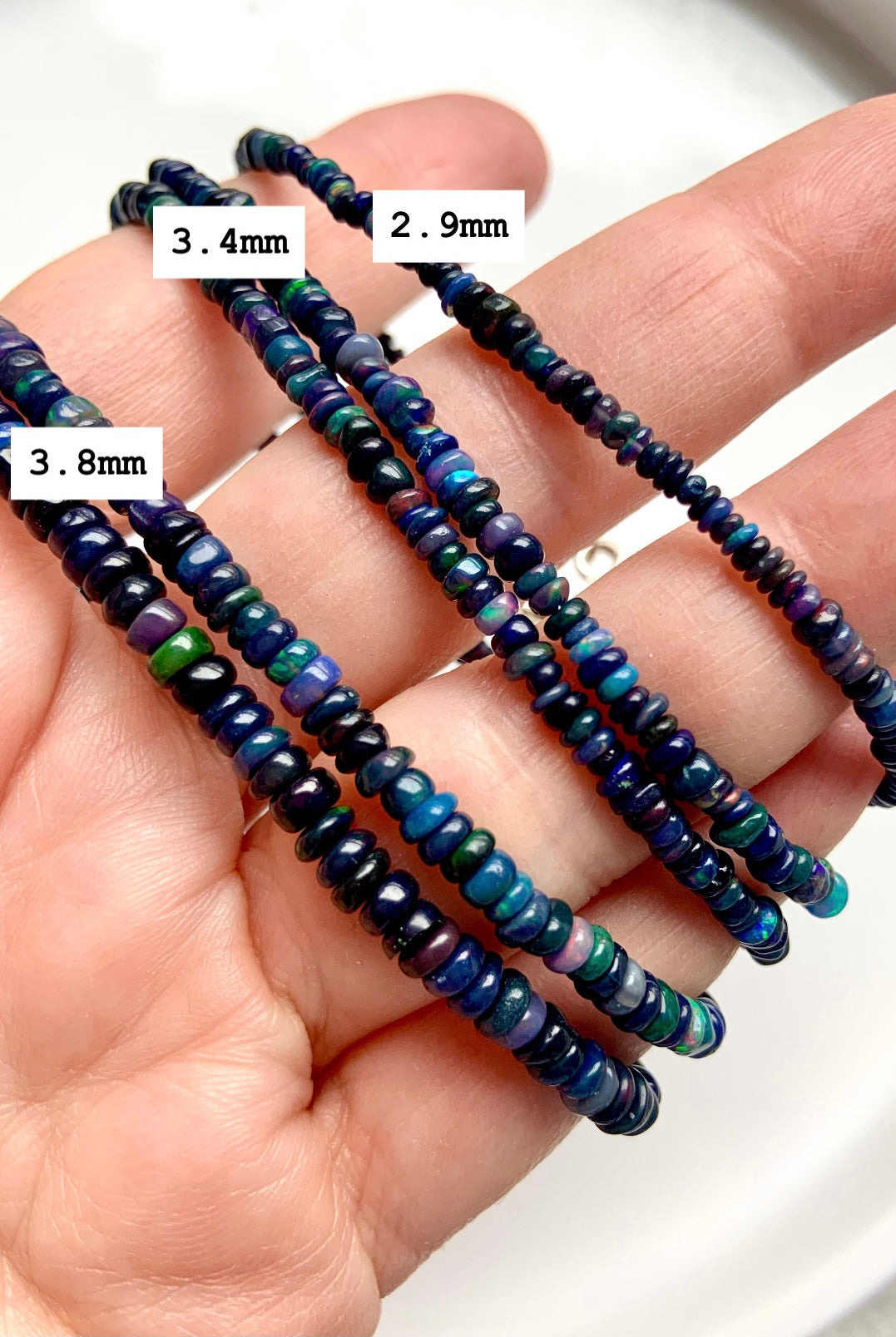 Three Black Fire Opal bracelets in bead sizes 2.9mm, 3.4mm, and 3.8mm displayed over a hand — size guide for opal bead jewelry.