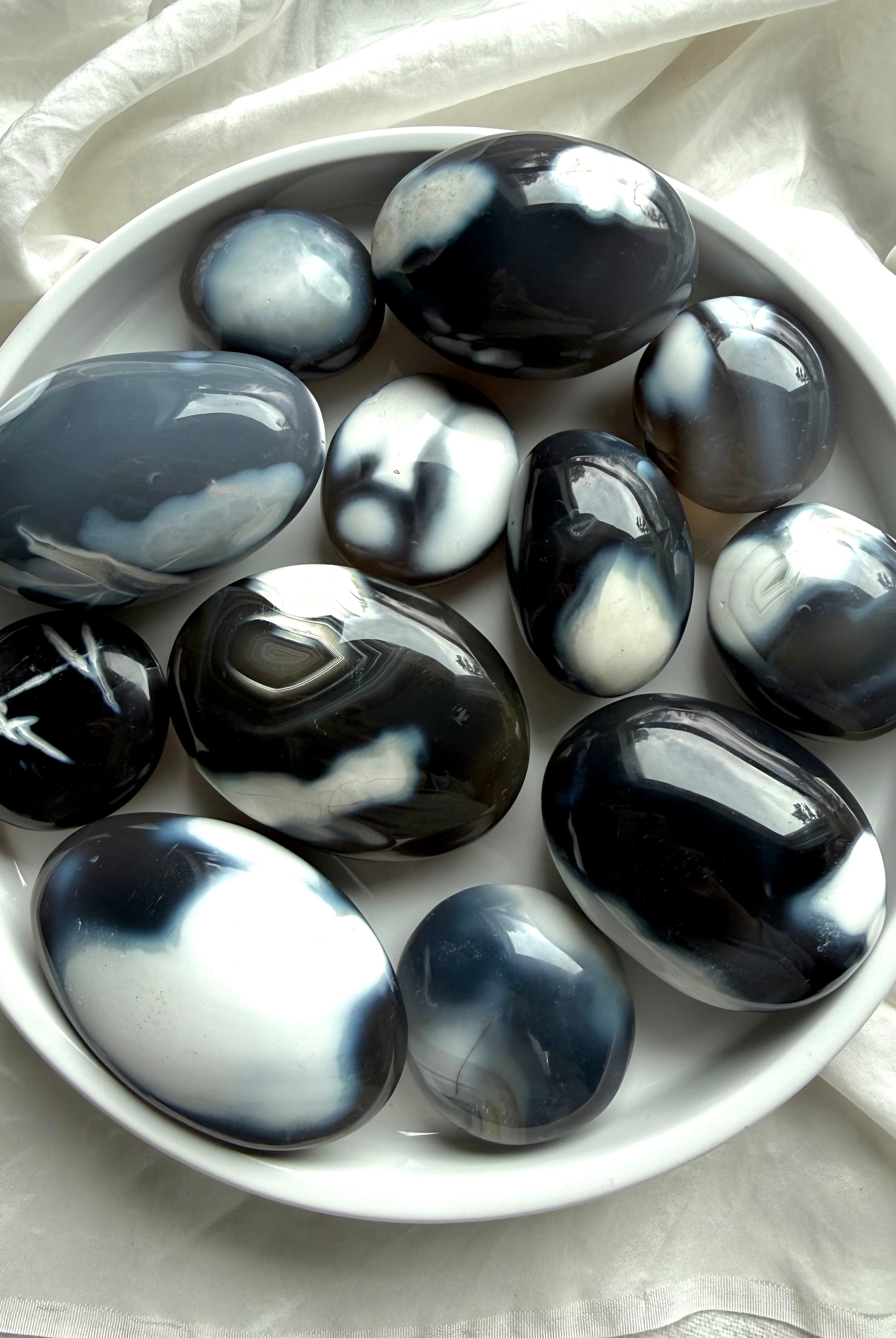Collection of polished Orca Agate palm stones in a white bowl, showcasing natural banding and soothing ocean-inspired tones