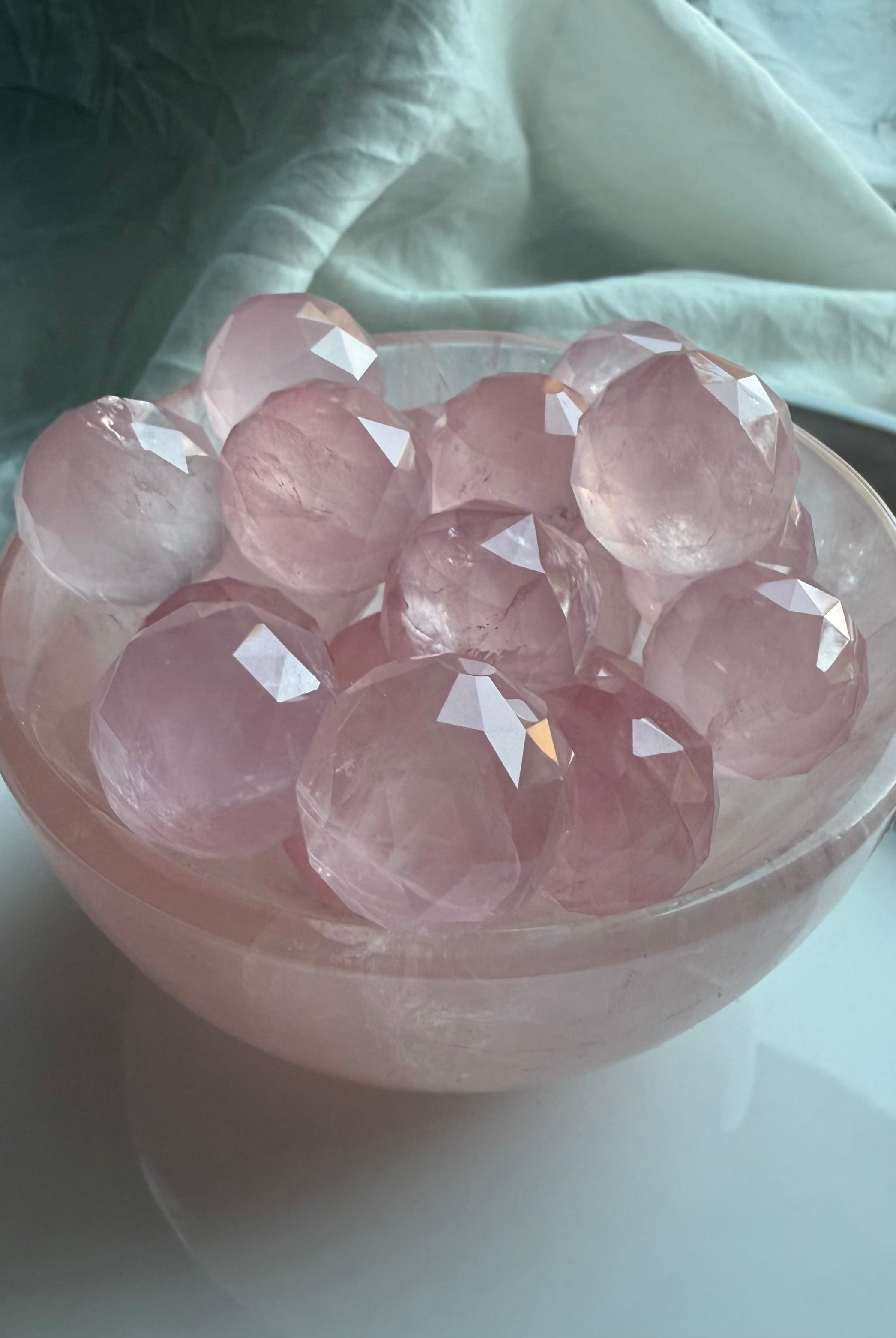 Glowing pink crystal balls in a rose quartz crystal bowl on a white surface. Calming crystals for peace.