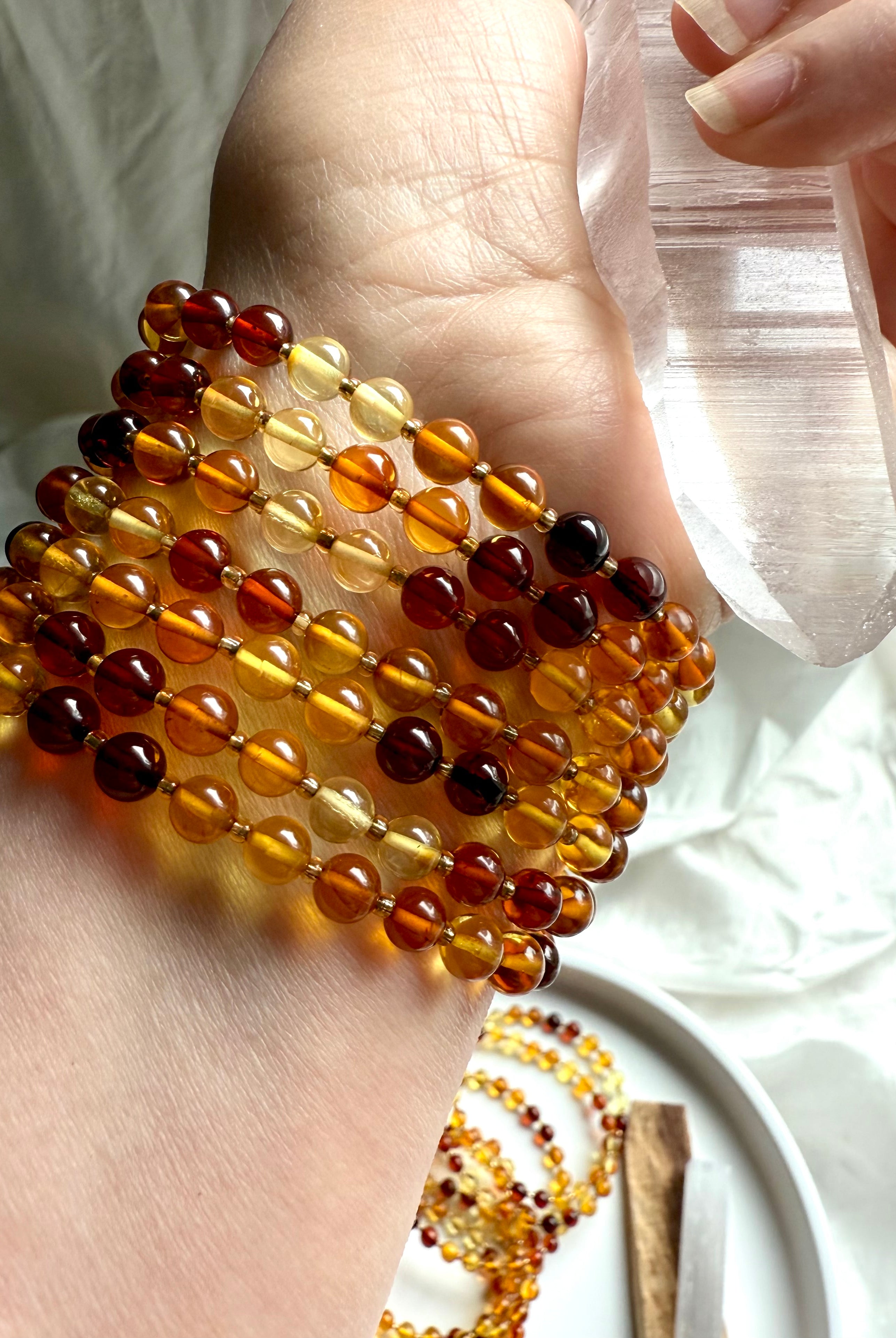 Stacked amber bead bracelets on wrist with Lemurian Quartz wand – radiant healing crystals for energy, warmth + clarity