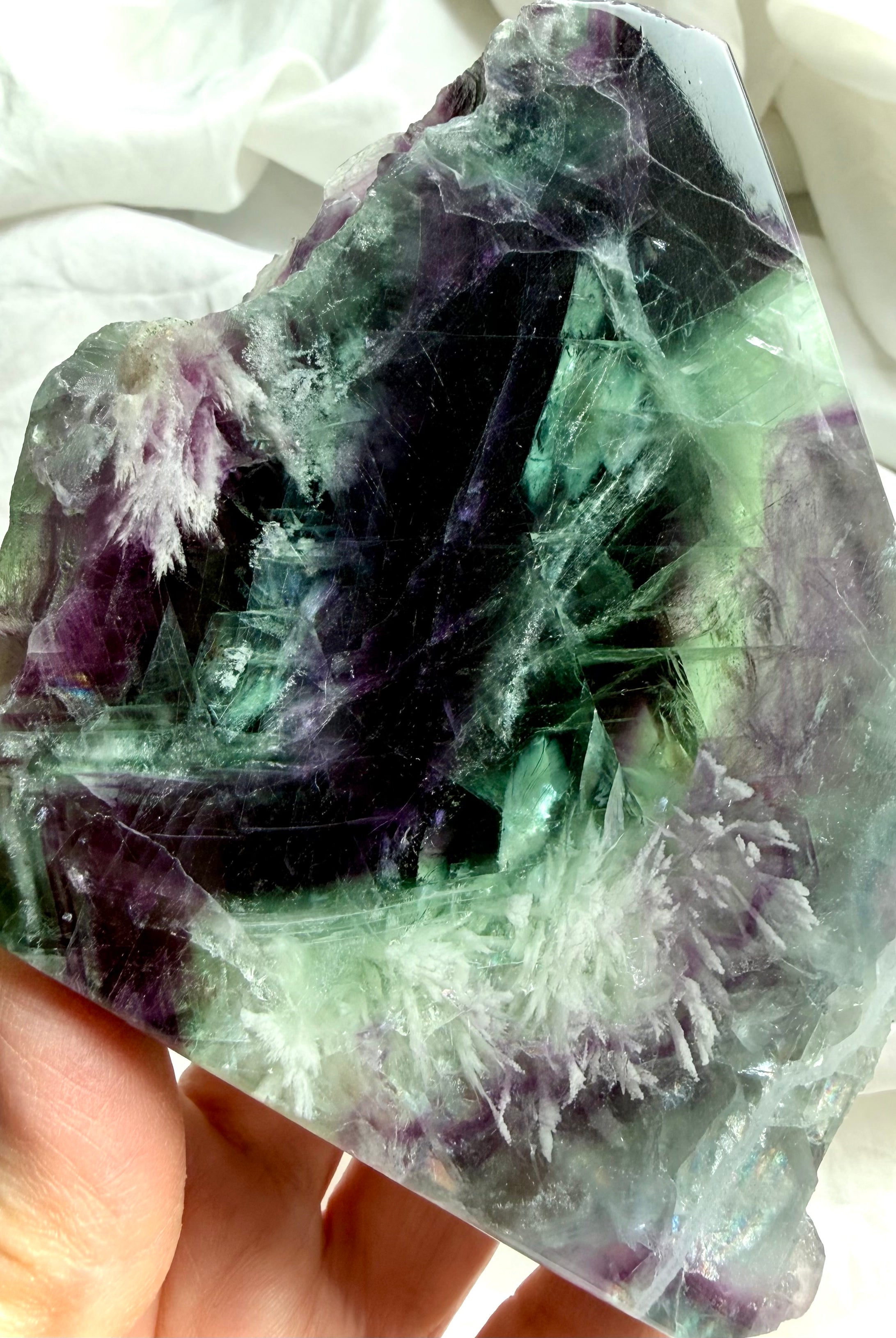 Polished fluorite slab photographed in natural light highlighting layered green and violet color zoning with rainbows