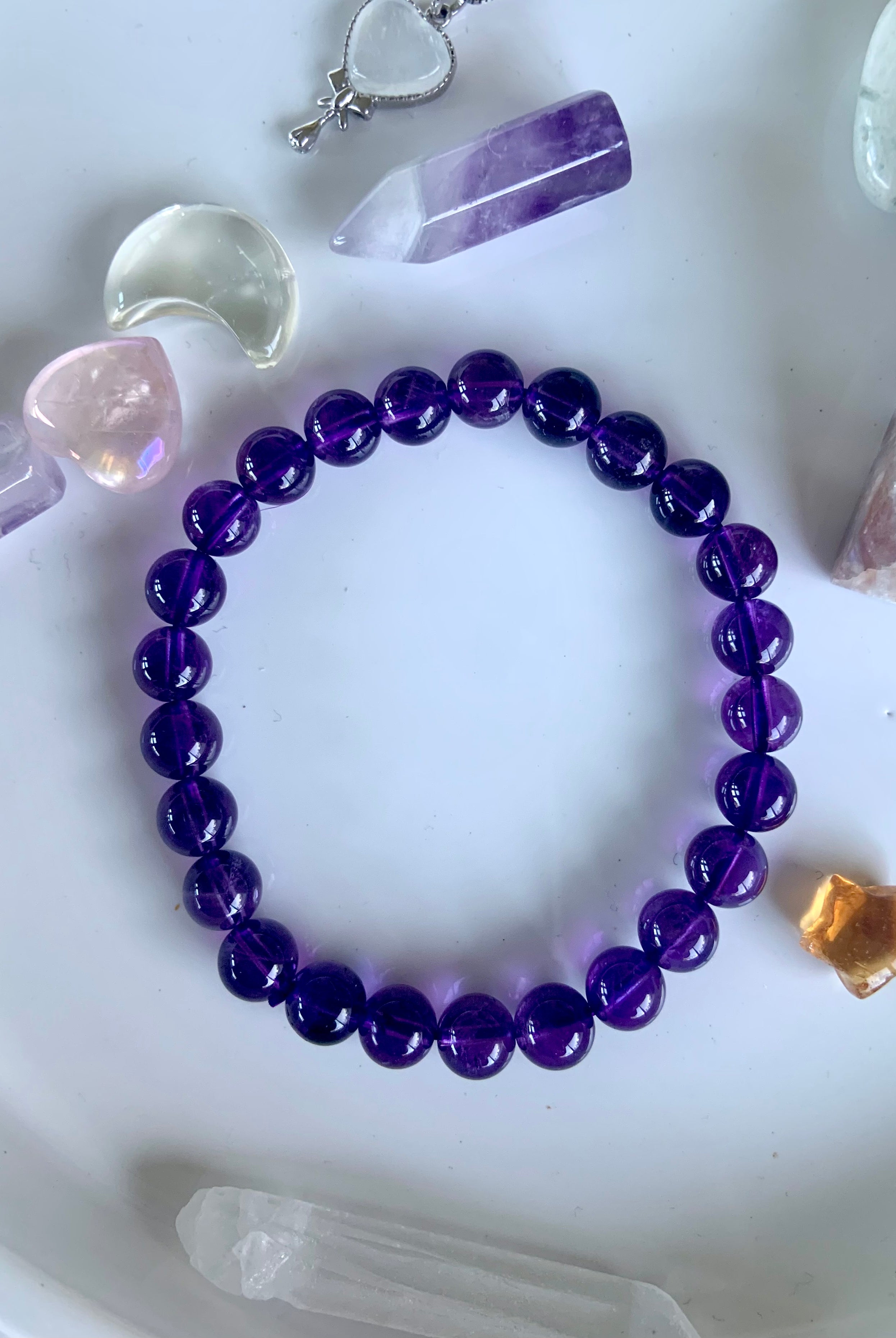 Overhead view of a deep purple amethyst crystal bracelet on a white plate with mini crystals in the background