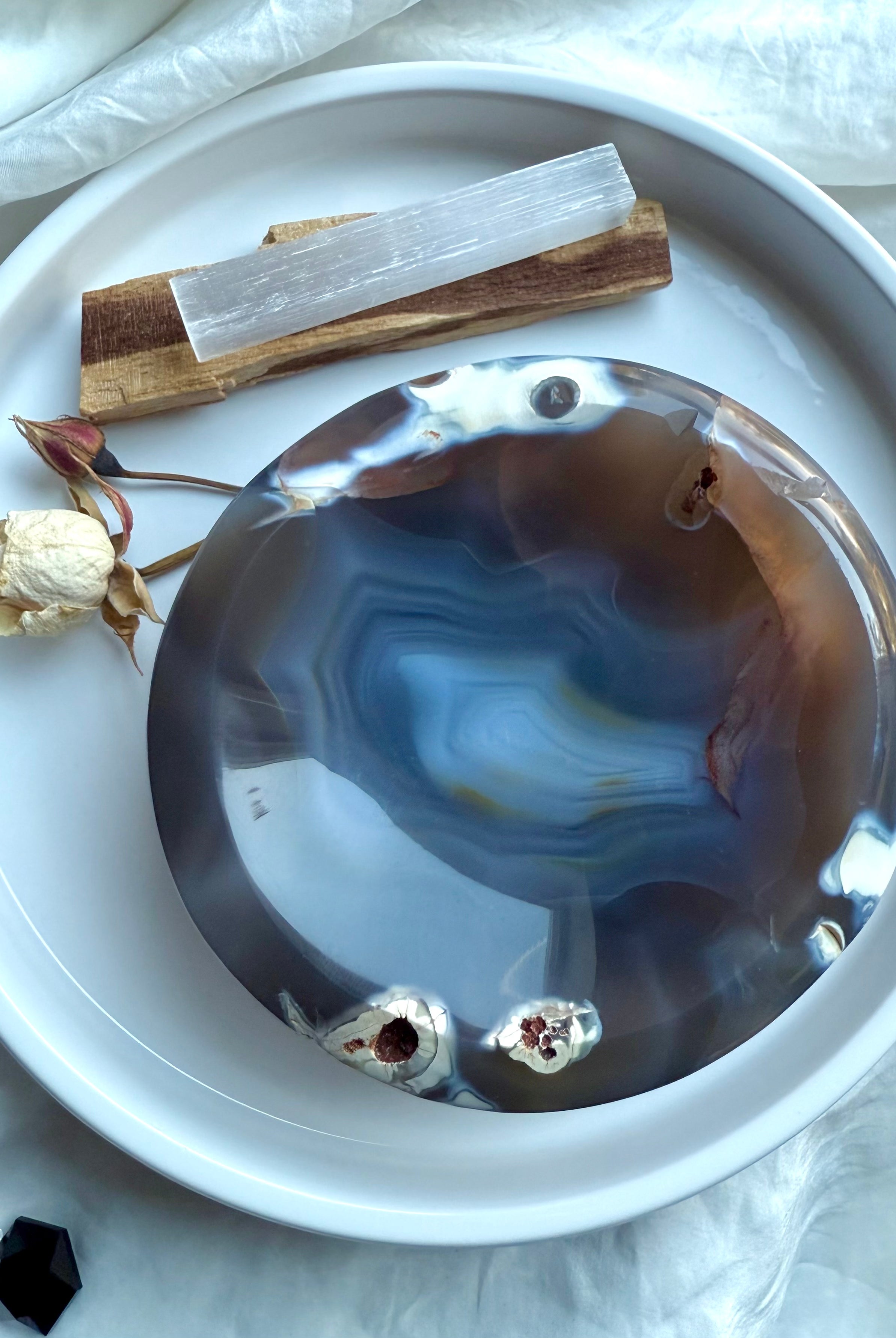 Orca Agate crystal bowl on white tray with selenite stick, palo santo, and dried flowers for cleansing rituals