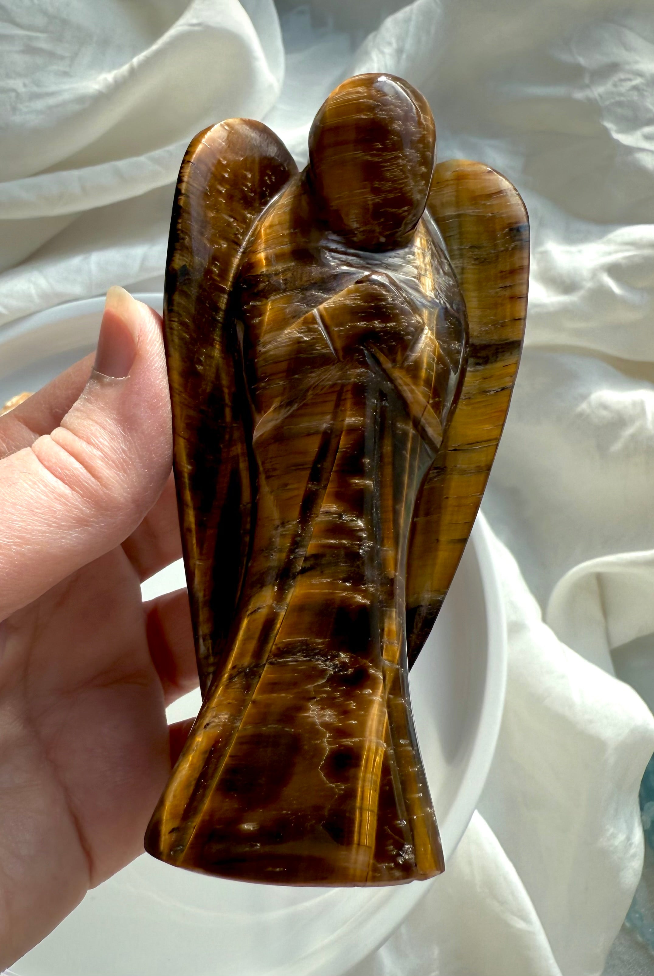 Front view of Golden Tiger’s Eye angel sculpture held in hand against soft white background