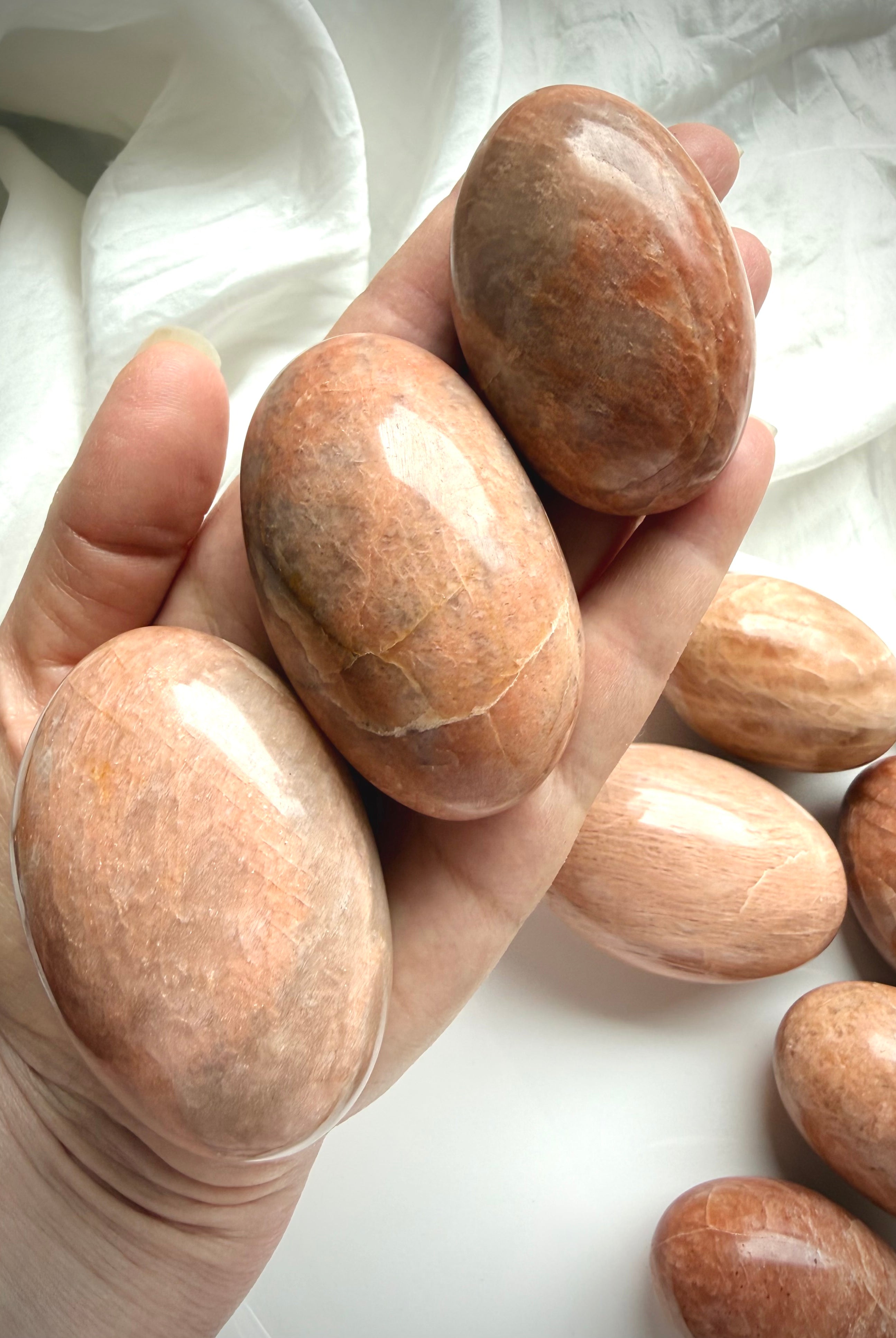 Hand holding large Peach Moonstone palm stones with warm peach tones, polished finish, and natural shimmer for meditation and emotional healing
