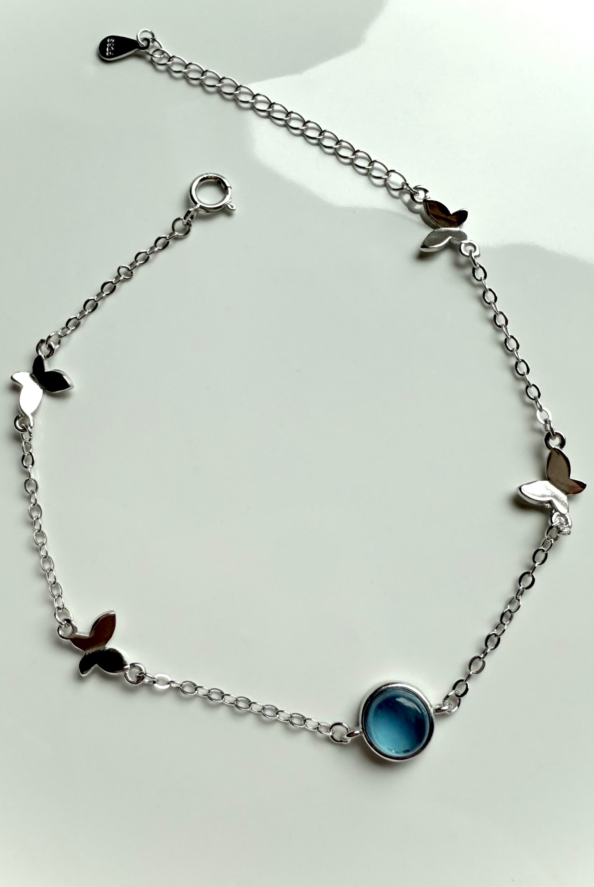 Delicate sterling silver bracelet with aquamarine crystal and butterfly charms shown on a white plate for high-vibe jewelry gifting