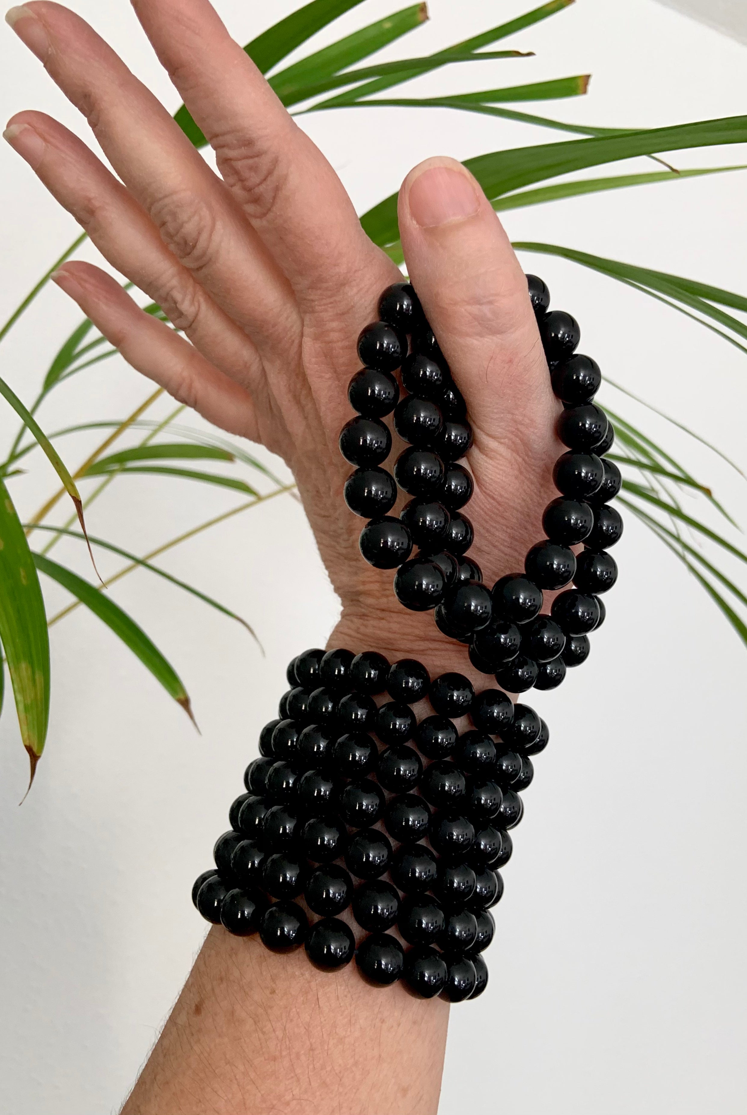 Stack of Black Tourmaline bracelets on wrist and held in hand with greenery in the background — natural setting for protective crystal jewelry