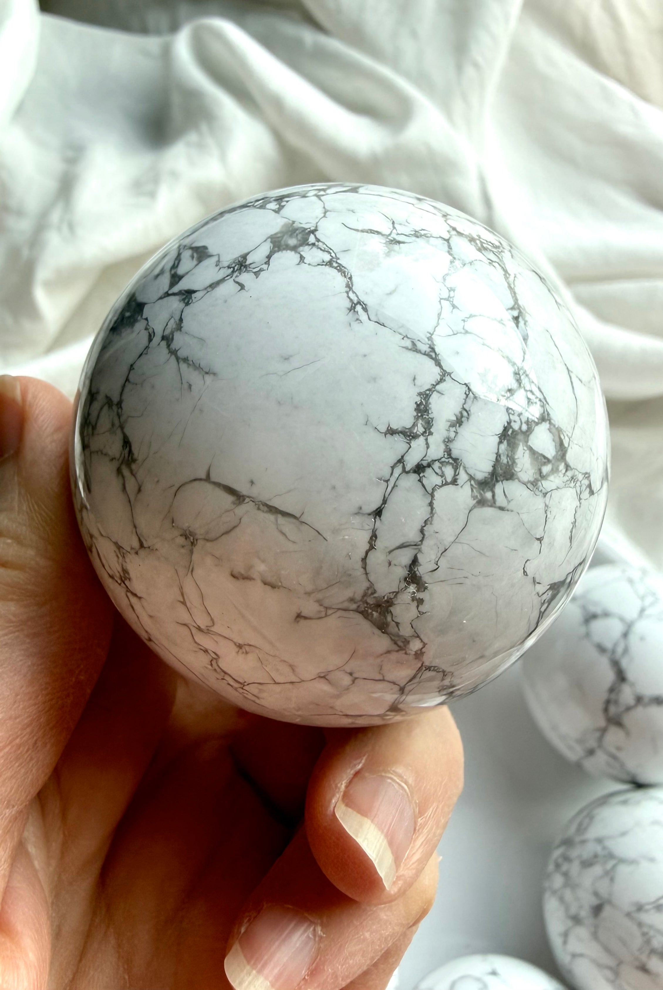 Close-up of Howlite crystal sphere in hand showing detailed gray veining on polished white stone, calming crystal for stress relief and peaceful energy