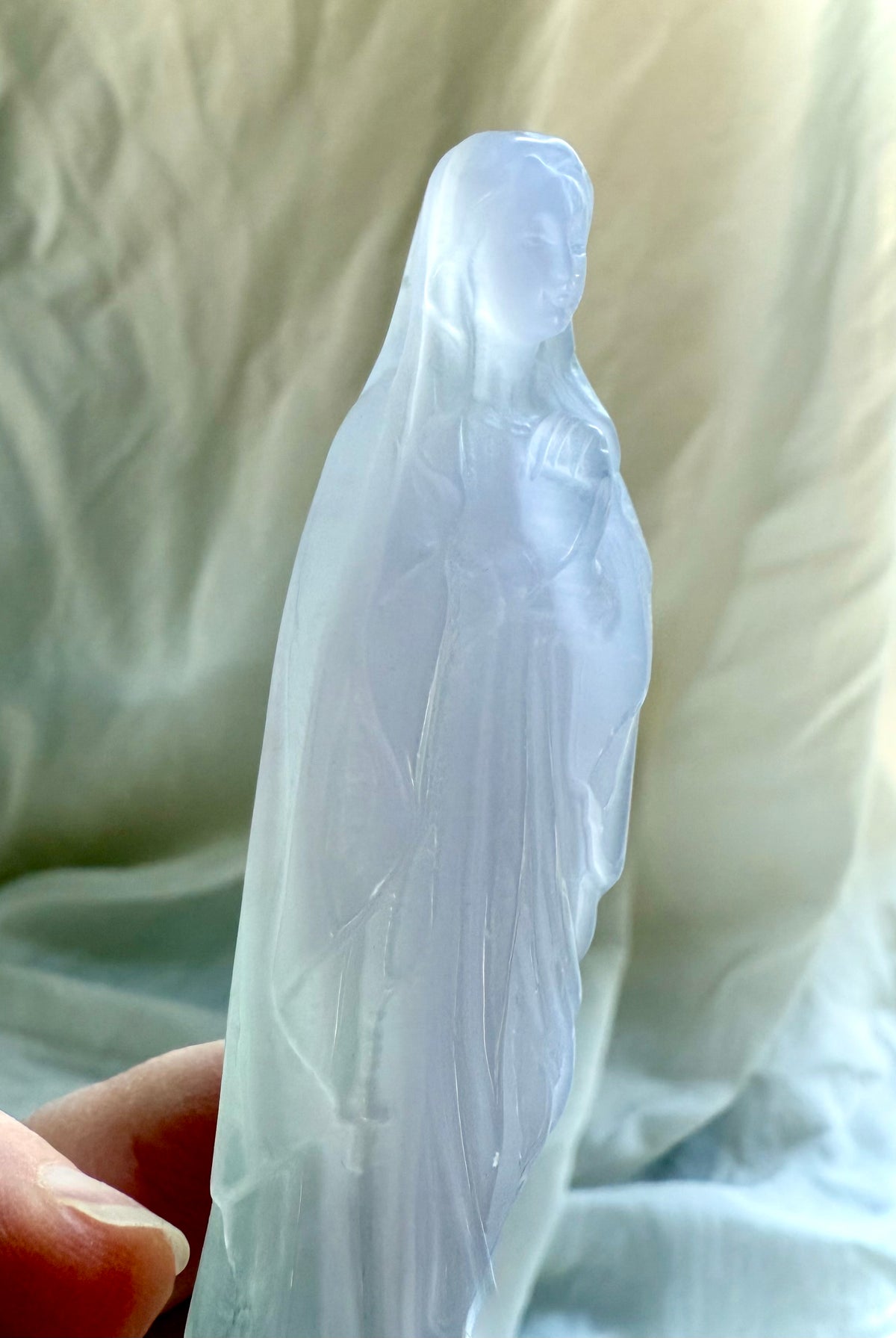 Mother Mary crystal statue in pale Lavender Fluorite, held in hand to show the carving’s size and delicate details