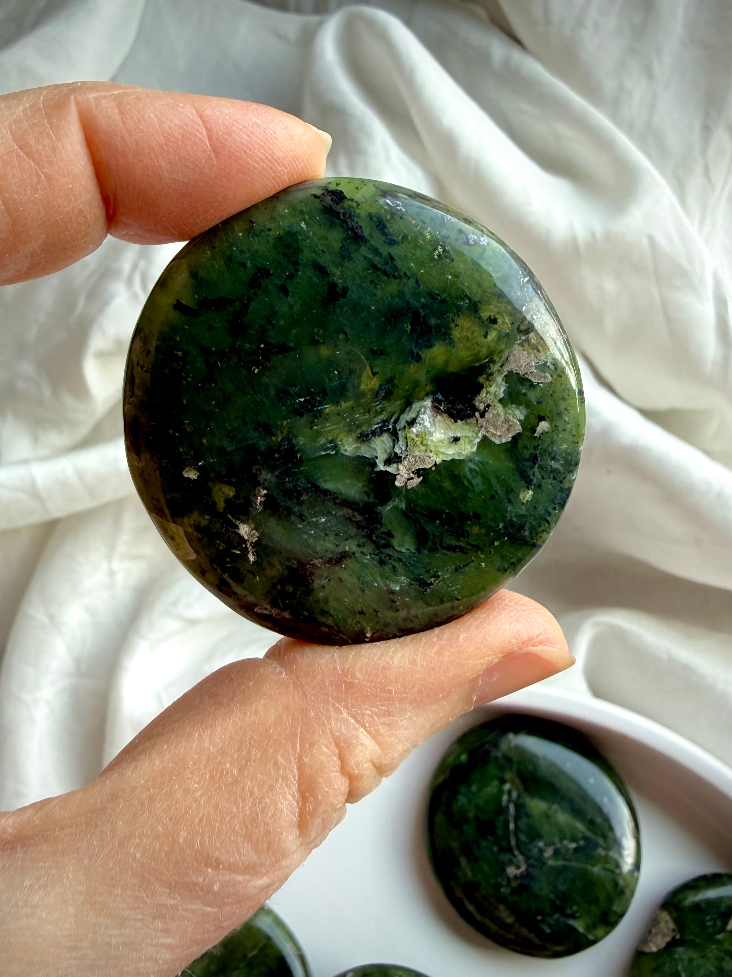 Closeup of nephrite jade palm stone held in hand, polished round green meditation crystal with natural marbling for heart chakra grounding