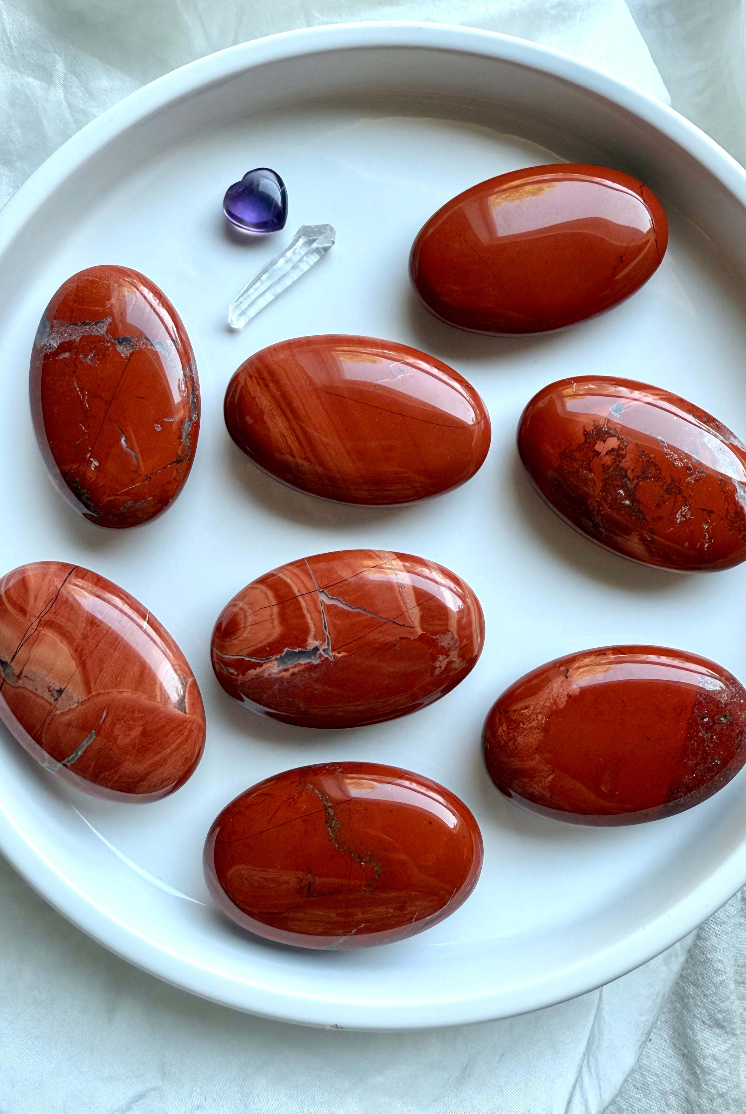 Flatlay of Red Jasper palm stones on white plate — smooth oval crystals with natural color variation.