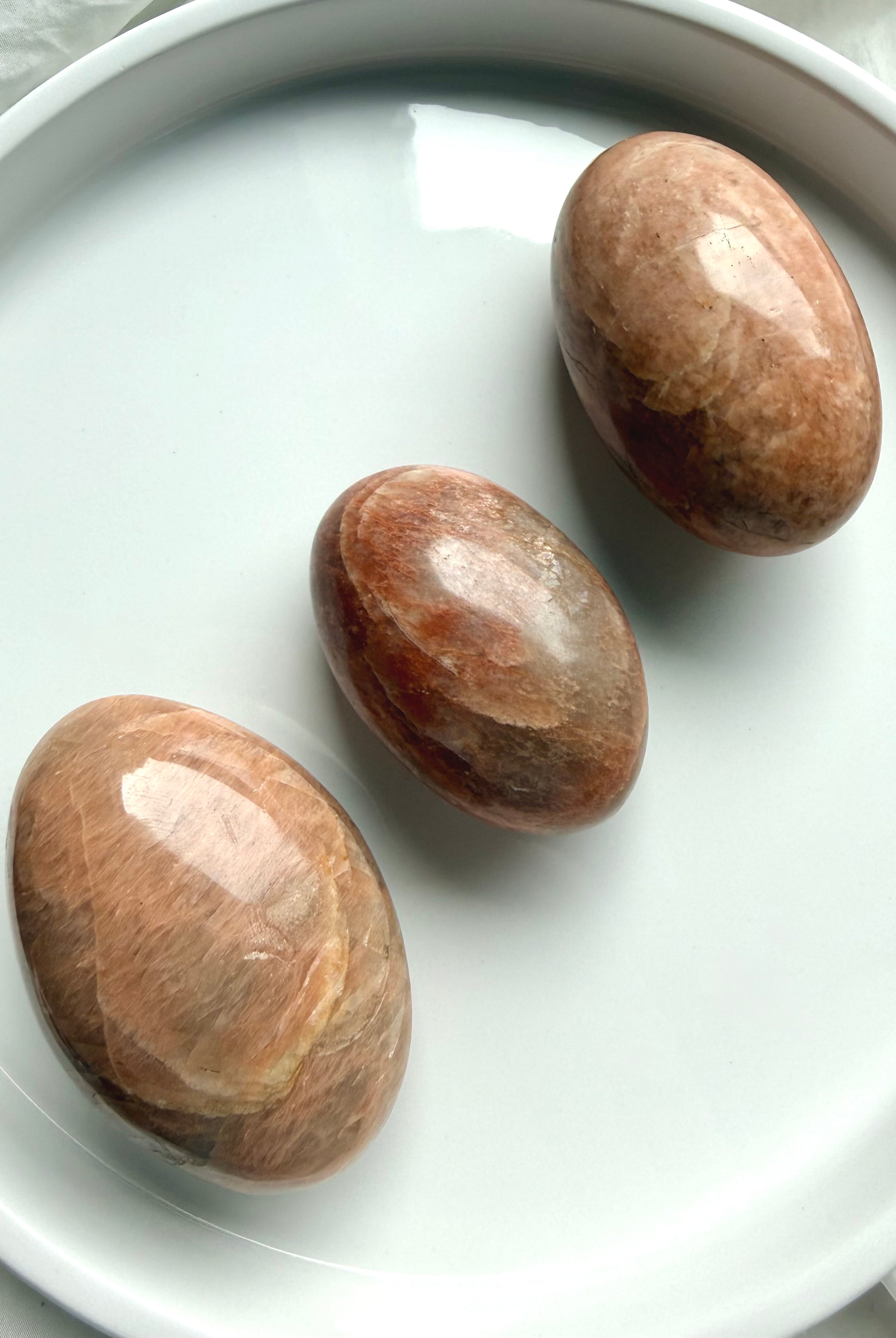 Three polished Peach Moonstone palm stones with rounded grounding shapes and warm feminine energy tones