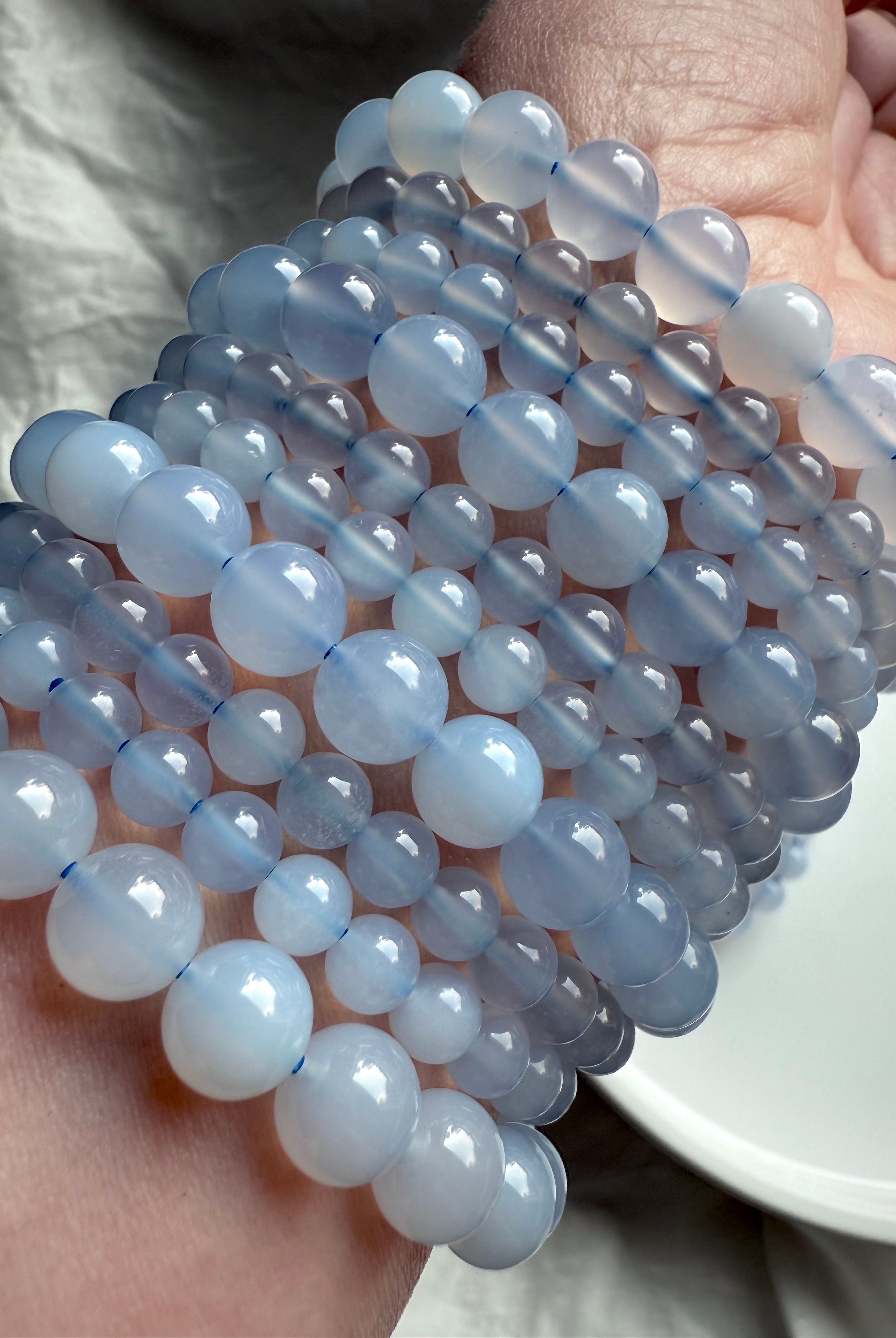 Glossy Blue Chalcedony bead bracelets in varied sizes layered on wrist — high-quality throat chakra crystal jewelry for peace