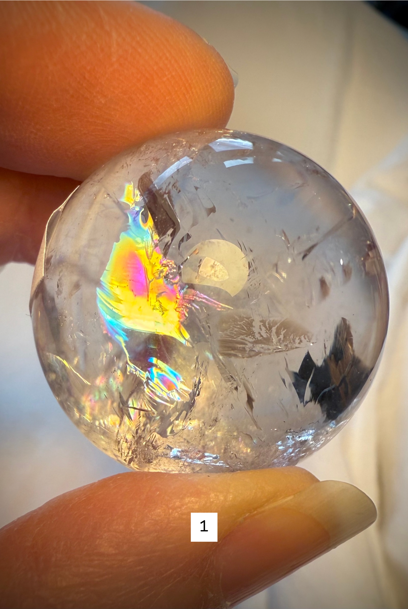 Close-up of Rainbow Quartz sphere #1 showing a vivid rainbow inclusion and clear crystalline structure.