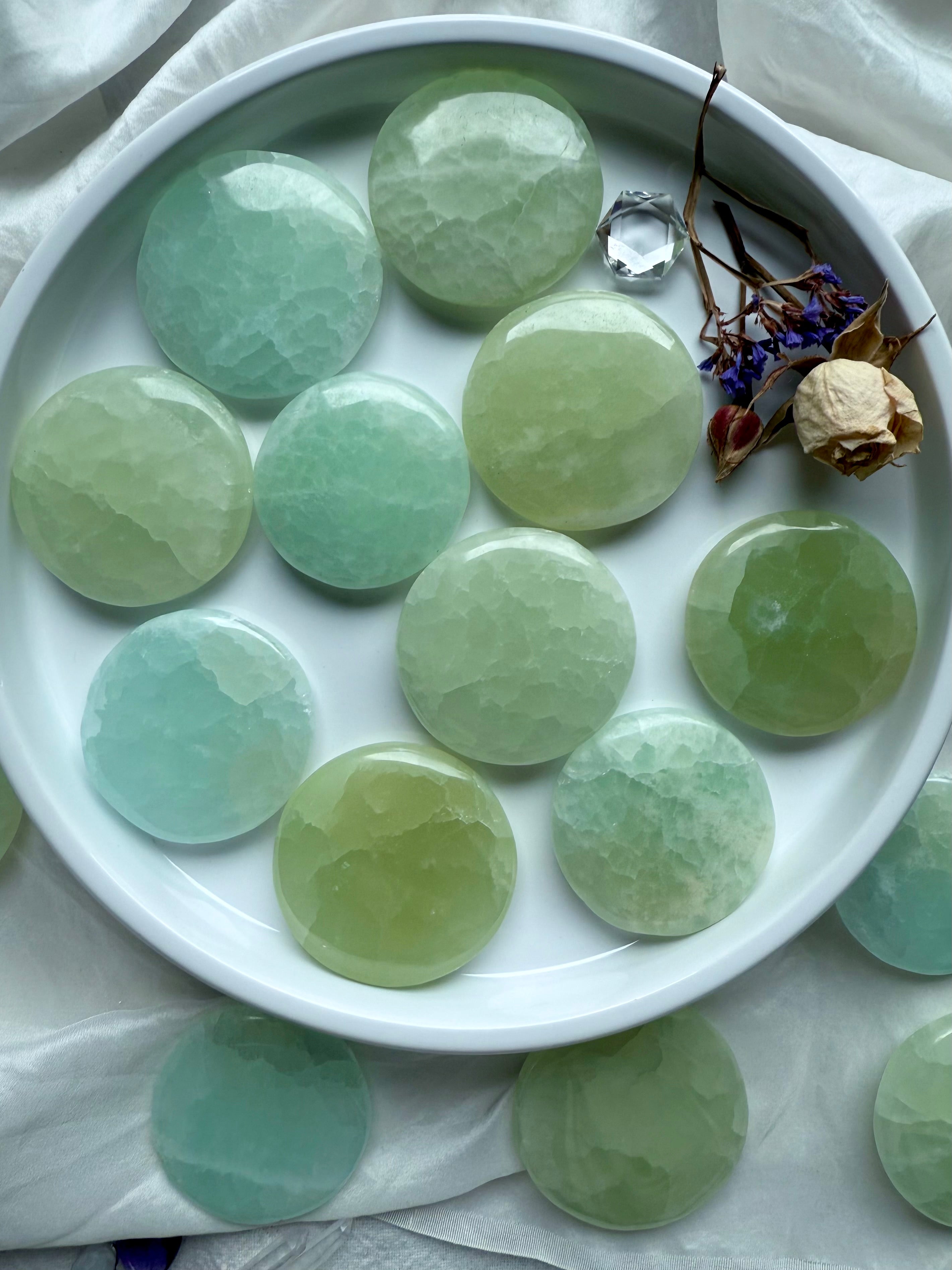 Flat lay of Pistachio Calcite meditation stones in soft green hues, arranged in a white dish with dried flowers