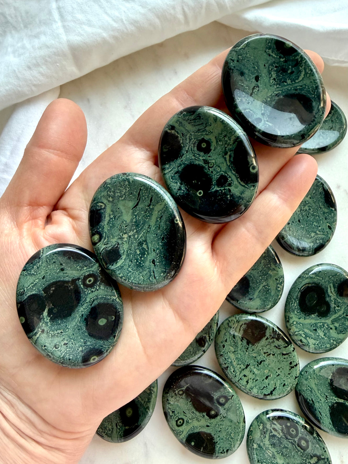 Kambaba Jasper worry stones held in hand showing polished oval shape, thumb indentation, and natural green orbicular patterns