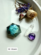 Flatlay of flashy Labradorite hexagon with clear quartz points, amethyst heart, and dried rose petals