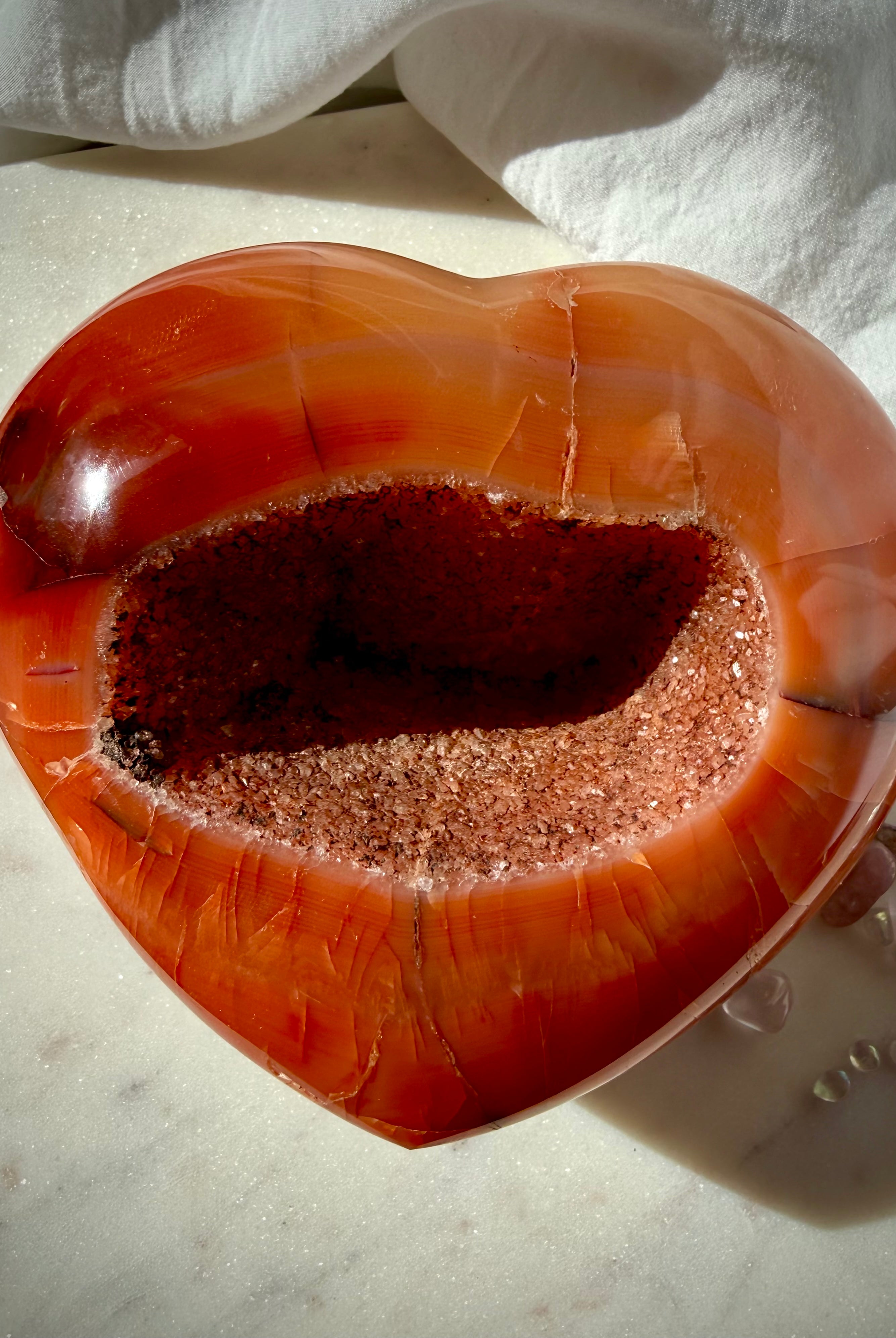 One of a kind Carnelian geode heart held in hand showcasing glittering druzy center and natural red-orange patterns