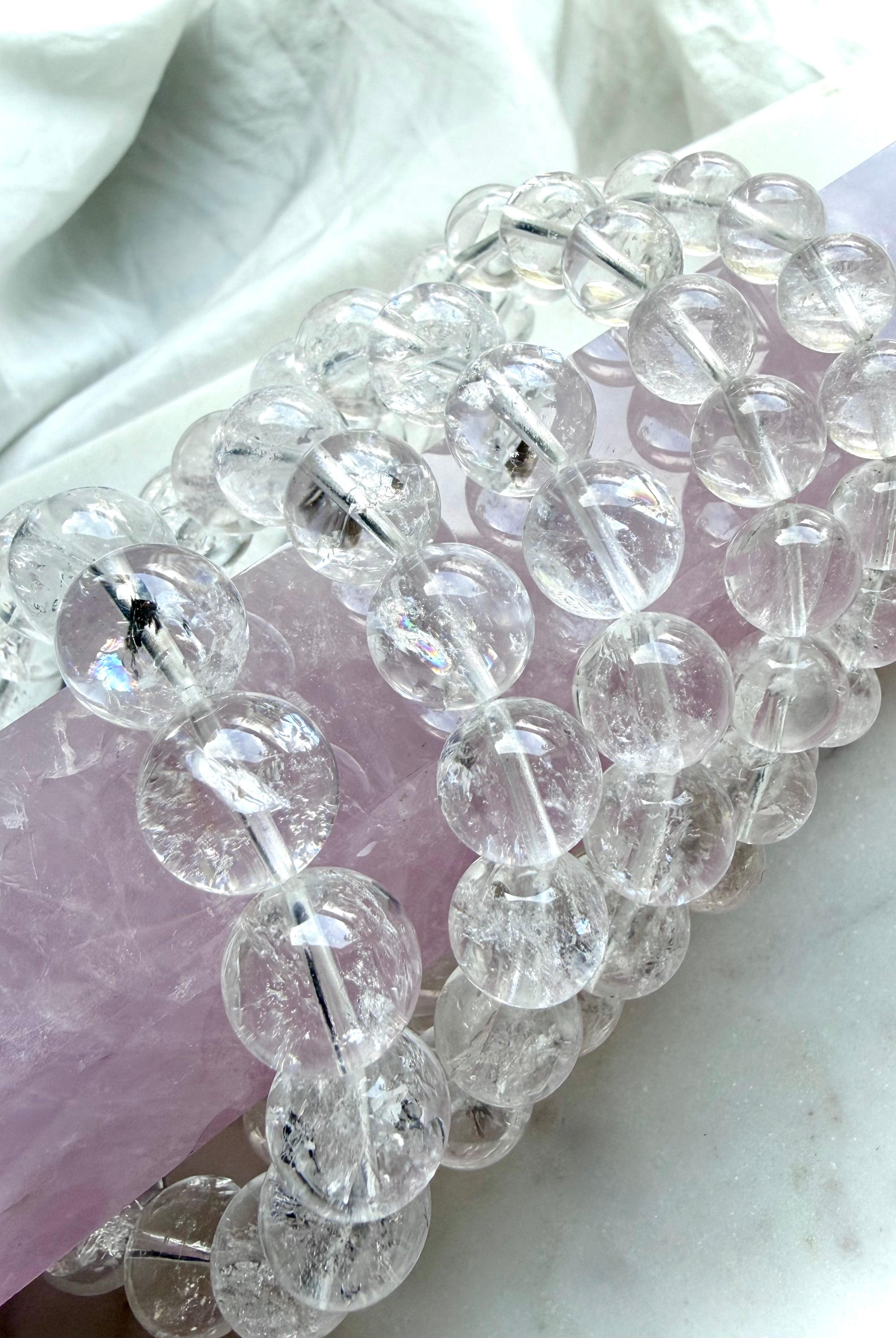 Rainbow Clear Quartz bracelet displayed on pink rose quartz with luminous transparent crystal beads