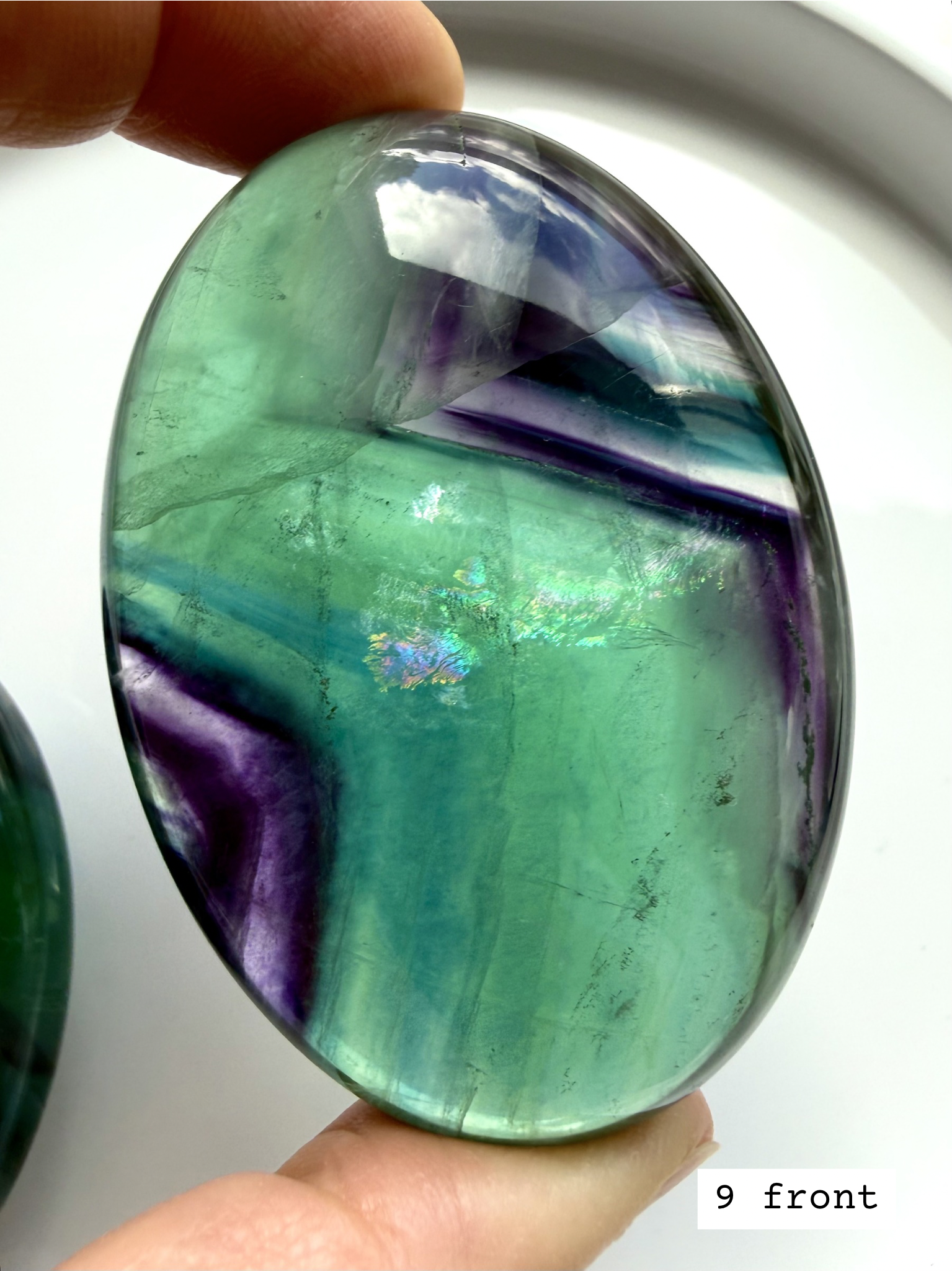 Teal fluorite palm stone #9 front held to the light, displaying translucent blue green bands and mineral variation