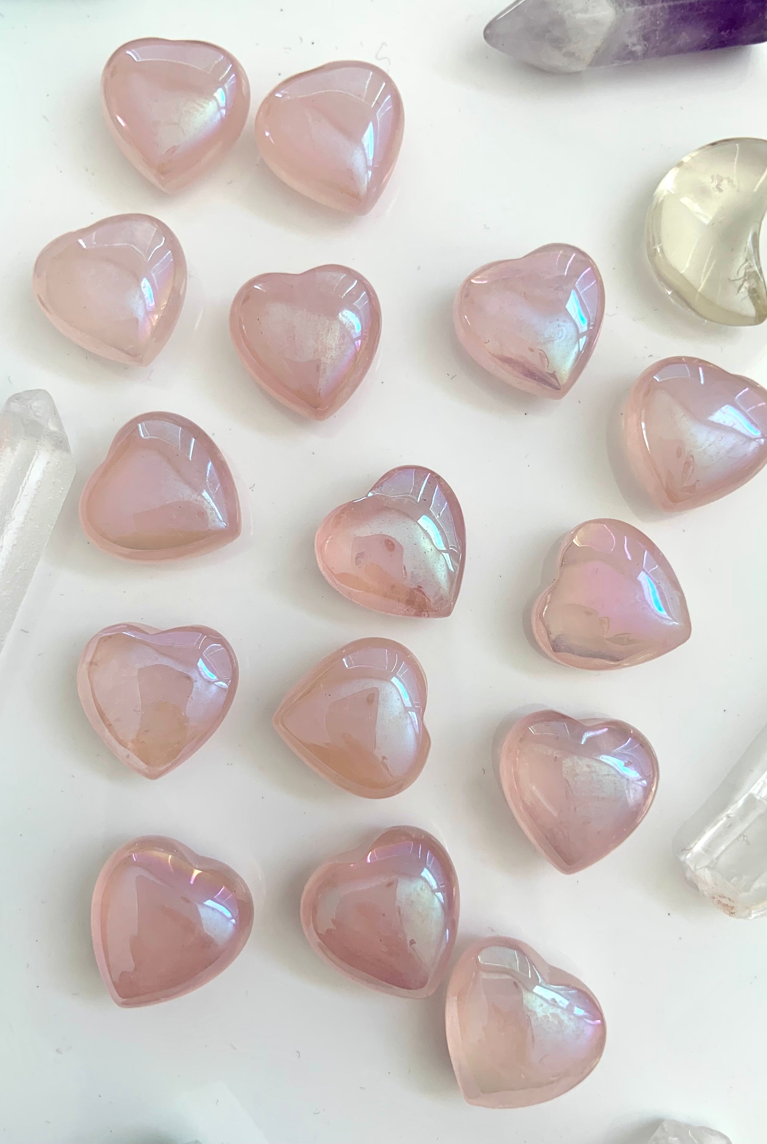 Flatlay of iridescent rose quartz aura hearts with other crystals on white — high-vibe pink crystals for love, peace, & spiritual connection