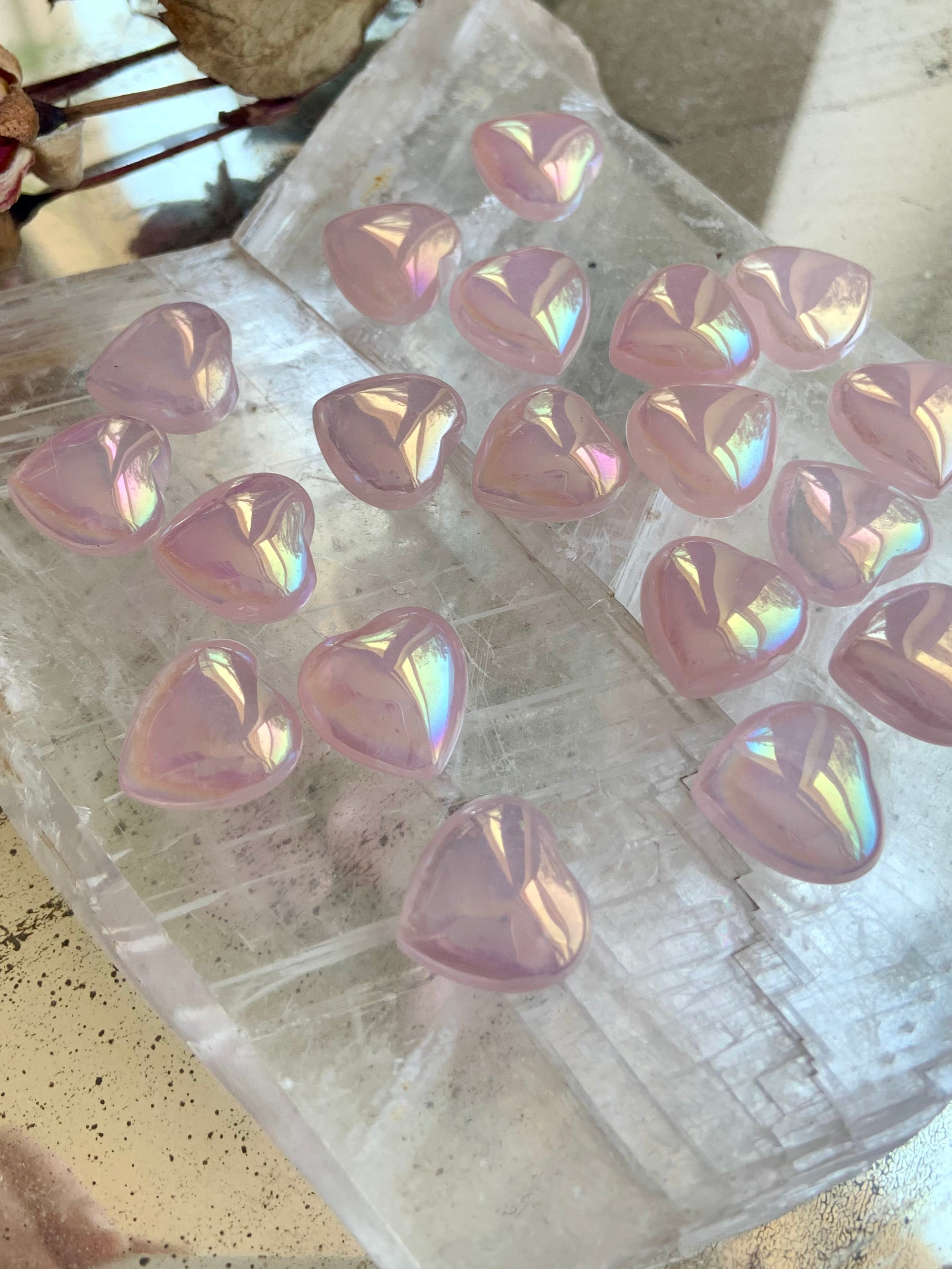 Close-up of mini aura rose quartz heart carvings on selenite slab showing iridescent pink crystal hearts