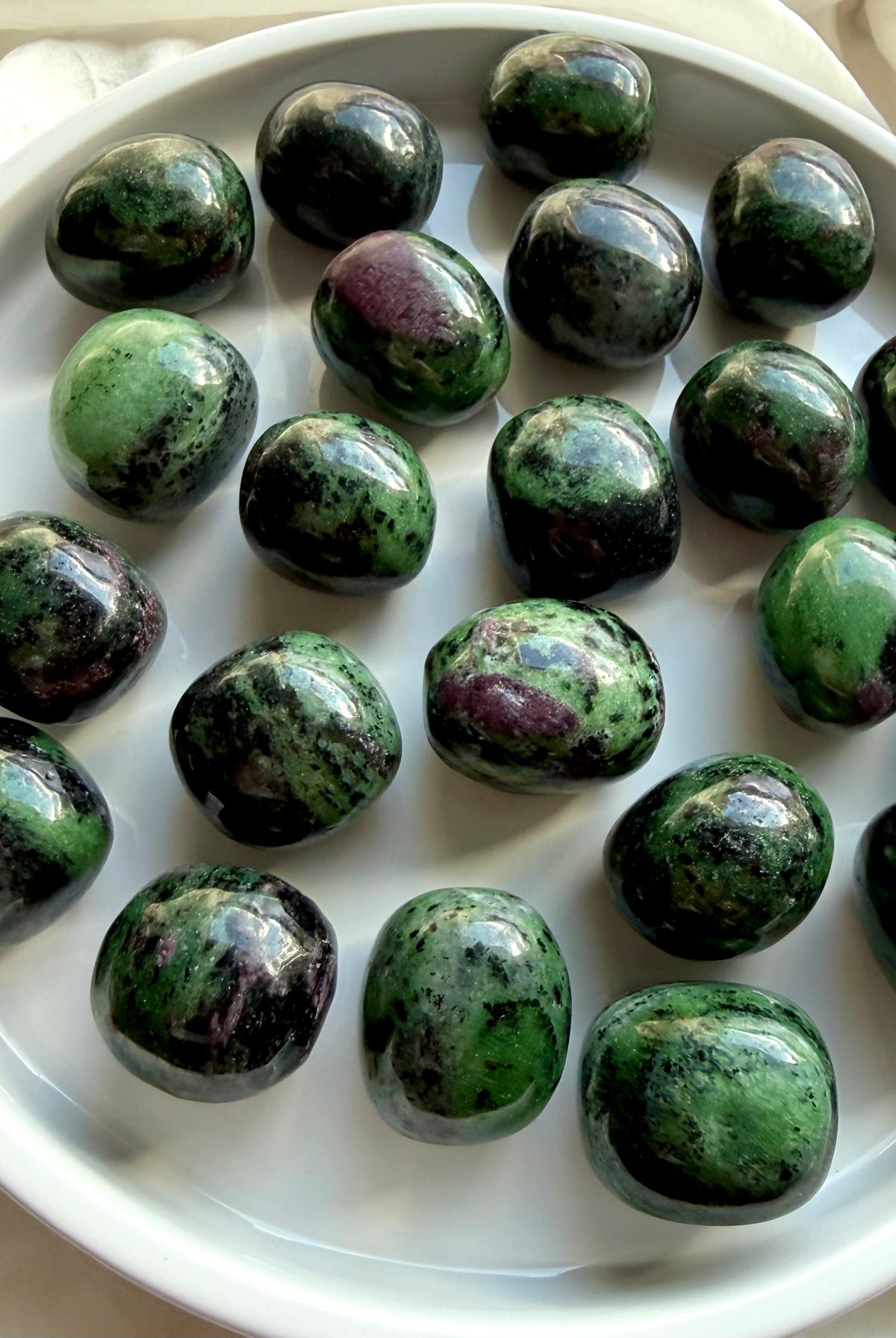 Collection of natural Anyolite tumbled stones in a white dish, green and ruby pink healing crystals for the Heart and Root Chakras