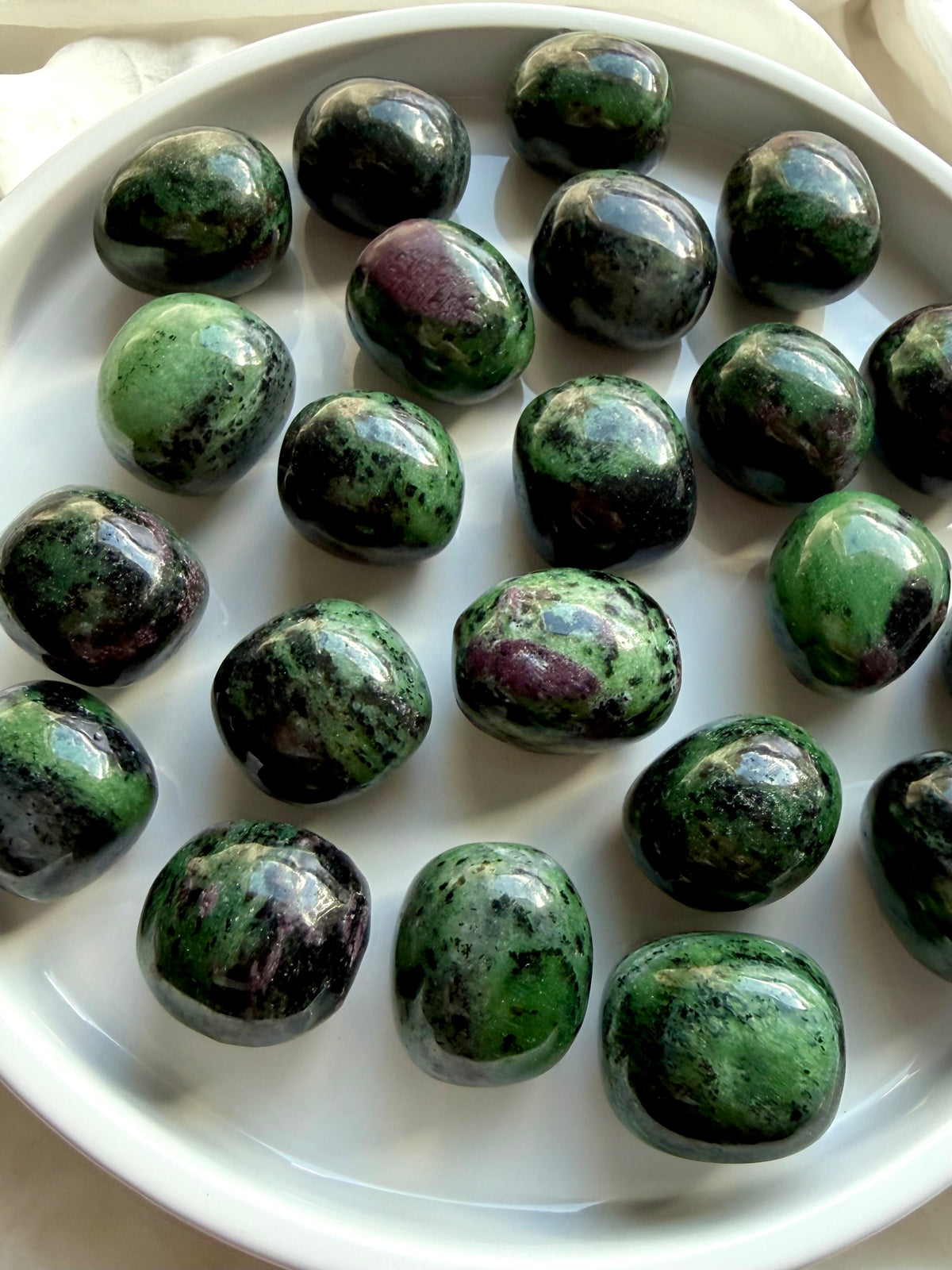 Collection of natural Anyolite tumbled stones in a white dish, green and ruby pink healing crystals for the Heart and Root Chakras