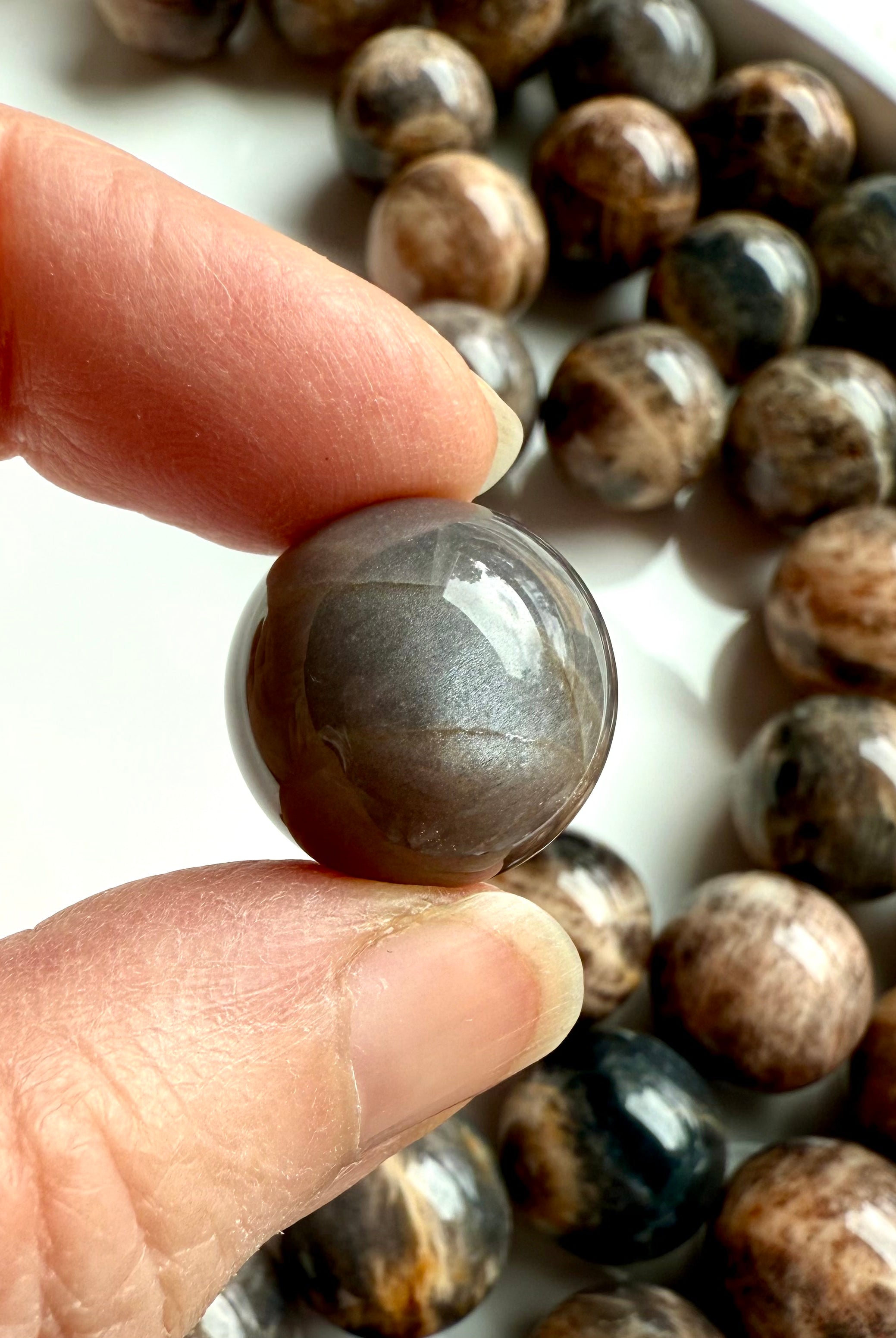 Closeup of a Black Moonstone sphere with dark, shimmery surface & chatoyancy for intuition, grounding, & emotional balance