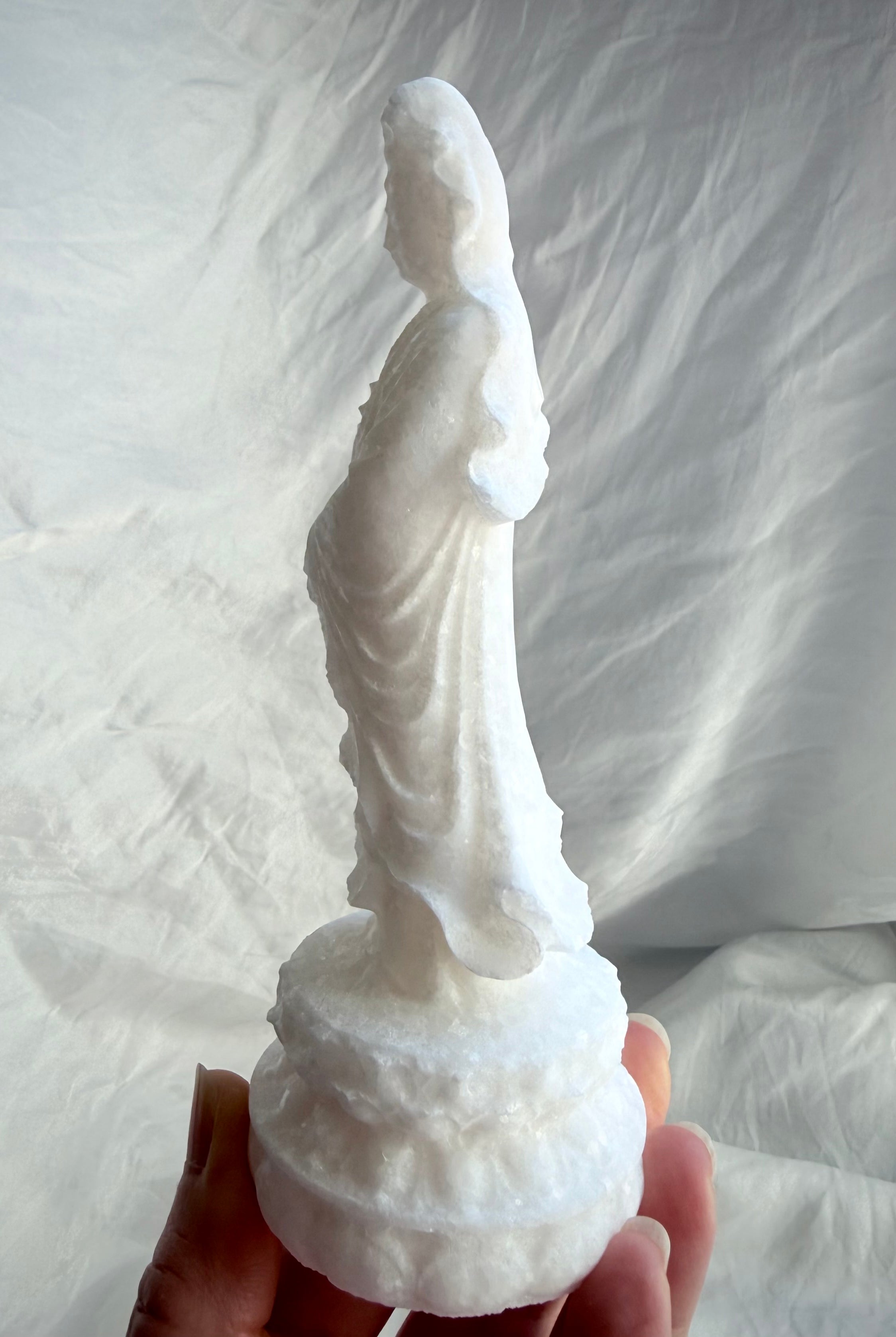 White Jade Standing Quan Yin statue held in hand from the side, showing flowing robes and natural crystalline sparkle