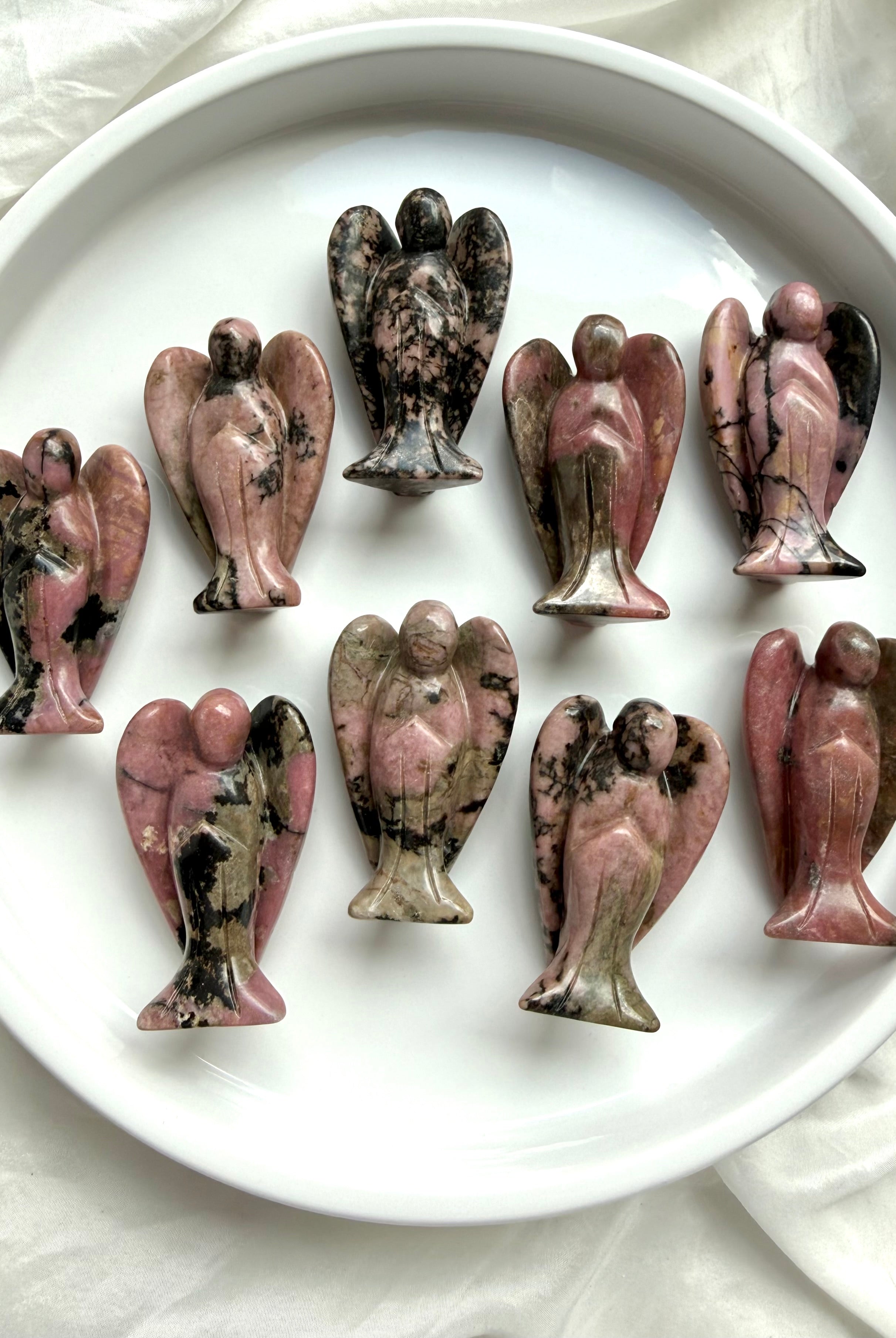 rhodonite angel carvings with pink and black natural patterns arranged on a white plate for heart healing and compassion