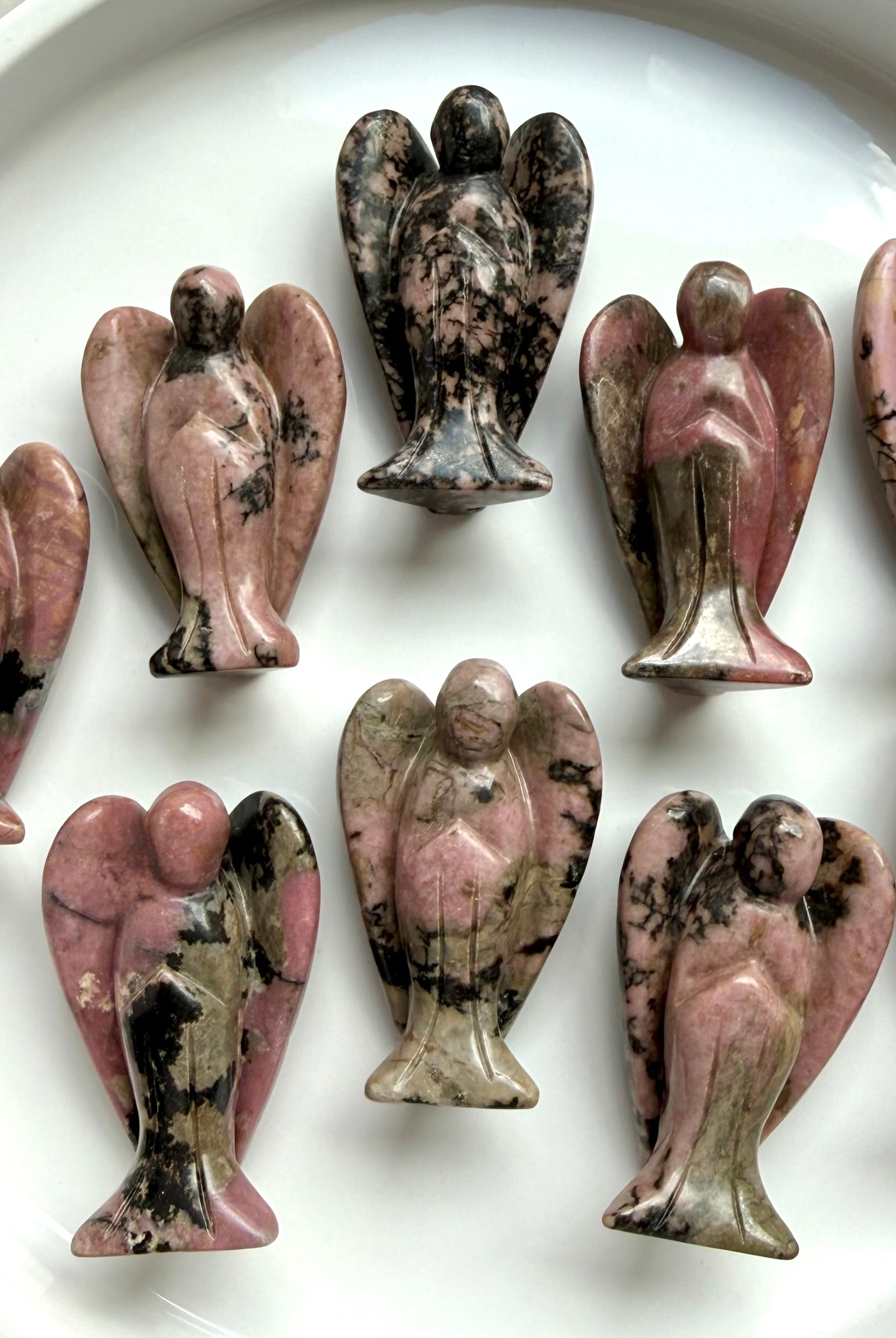 Collection of Rhodonite angel figurines with pink, black, and tan hues on a white surface