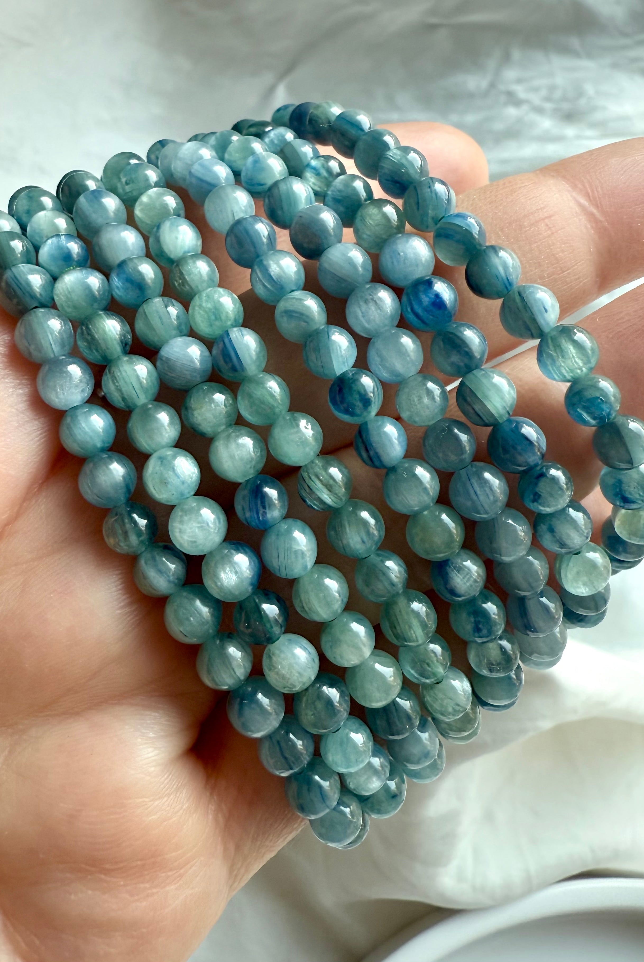 hand holding multiple blue-green kyanite crystal bracelets with radiant aqua, teal, and forest hues for intuition and spiritual clarity